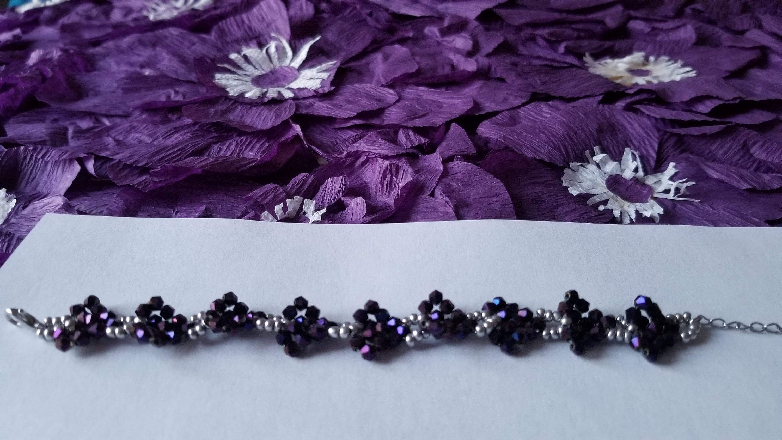 A stylish purple beaded bracelet featuring sparkly purple and silver beads arranged in a heart-shaped pattern on a stainless steel chain.