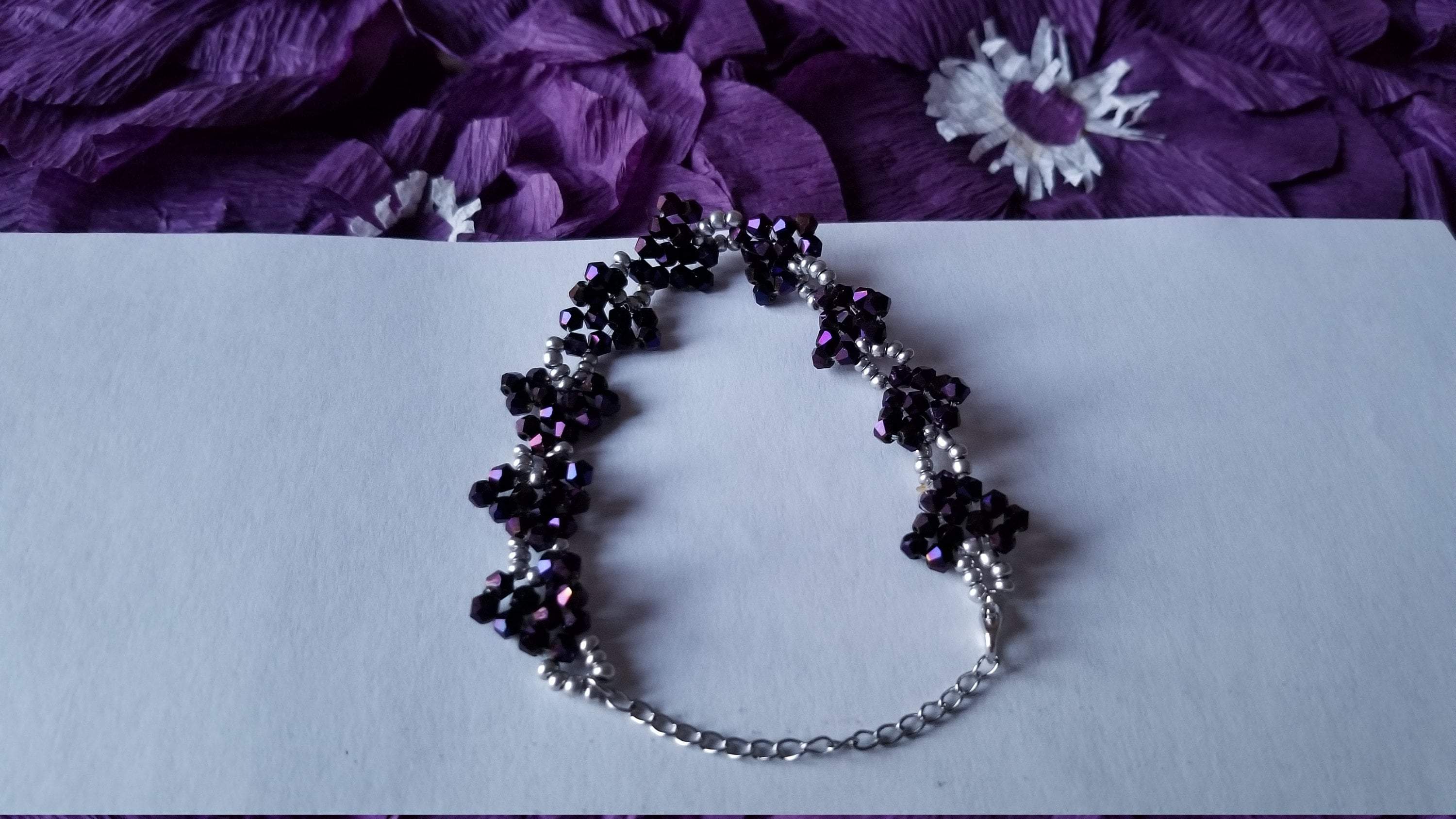 A stylish purple beaded bracelet featuring sparkly purple and silver beads arranged in a heart-shaped pattern on a stainless steel chain.