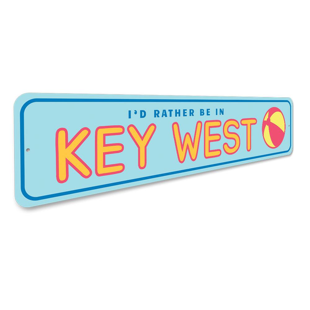 A decorative metal sign reading 'Rather Be in Key West', featuring vibrant colors and a beach-themed design, perfect for coastal decor.