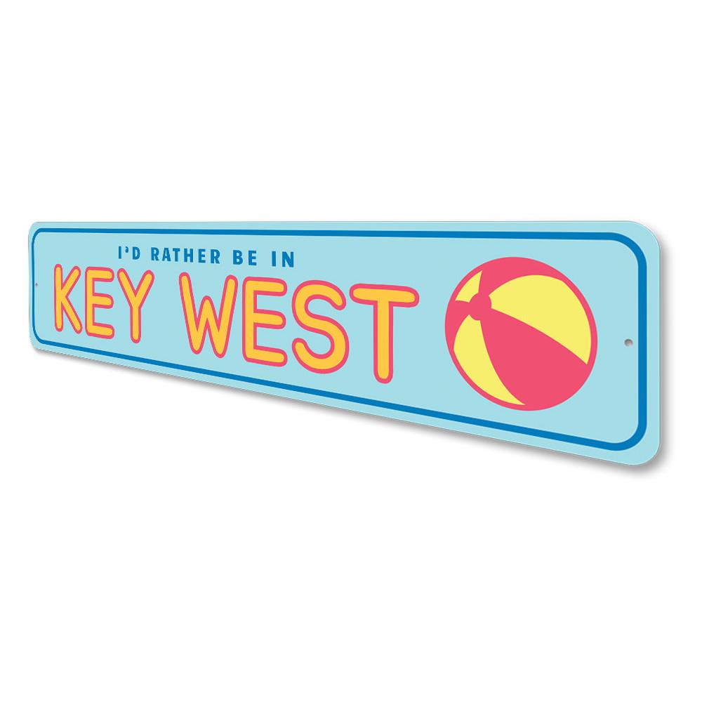 A decorative metal sign reading 'Rather Be in Key West', featuring vibrant colors and a beach-themed design, perfect for coastal decor.