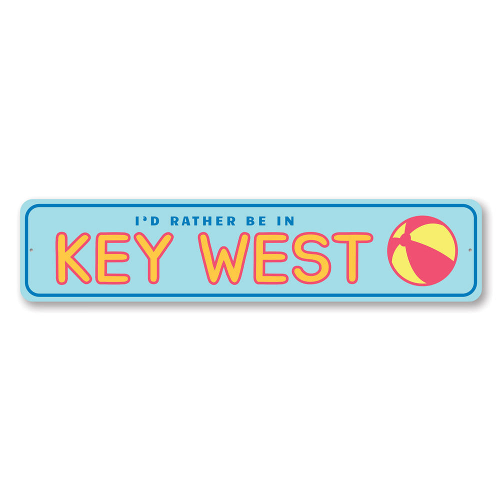 A decorative metal sign reading 'Rather Be in Key West', featuring vibrant colors and a beach-themed design, perfect for coastal decor.