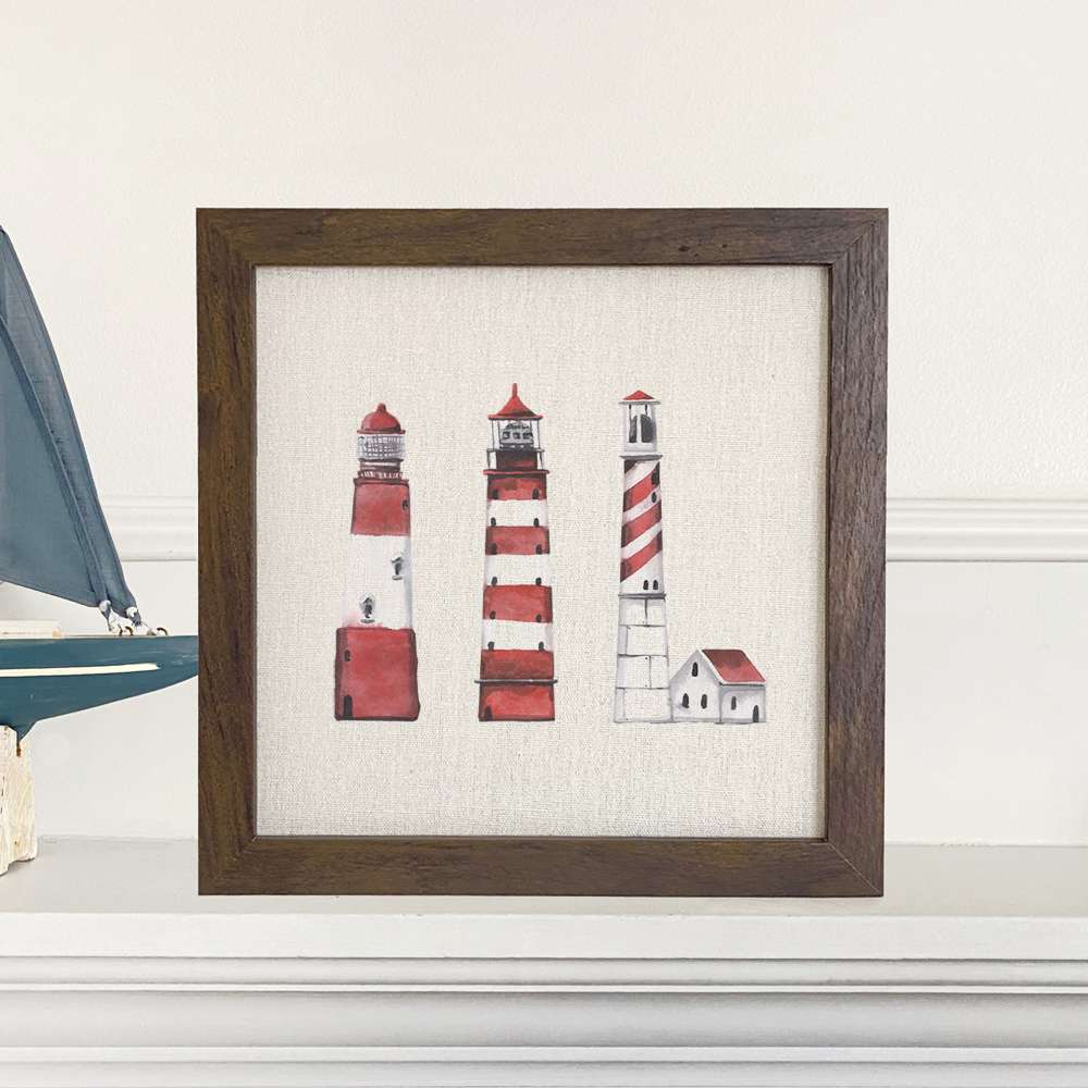 A beautifully framed sign featuring red lighthouses on a linen-look background, perfect for home decor.