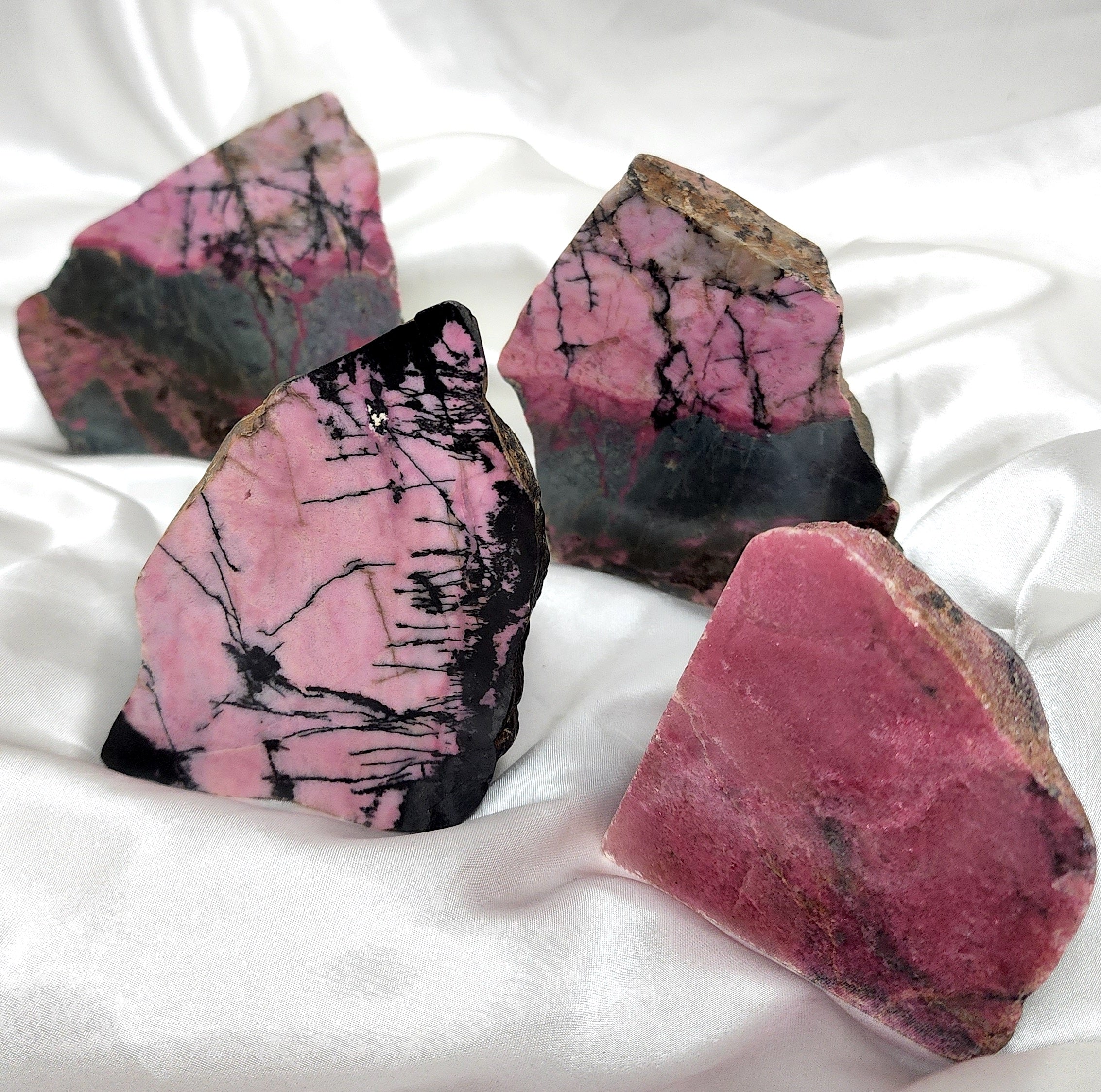 A collection of unique Rhodonite Freeform Slabs showcasing their pink and black patterns, perfect for emotional healing and decoration.