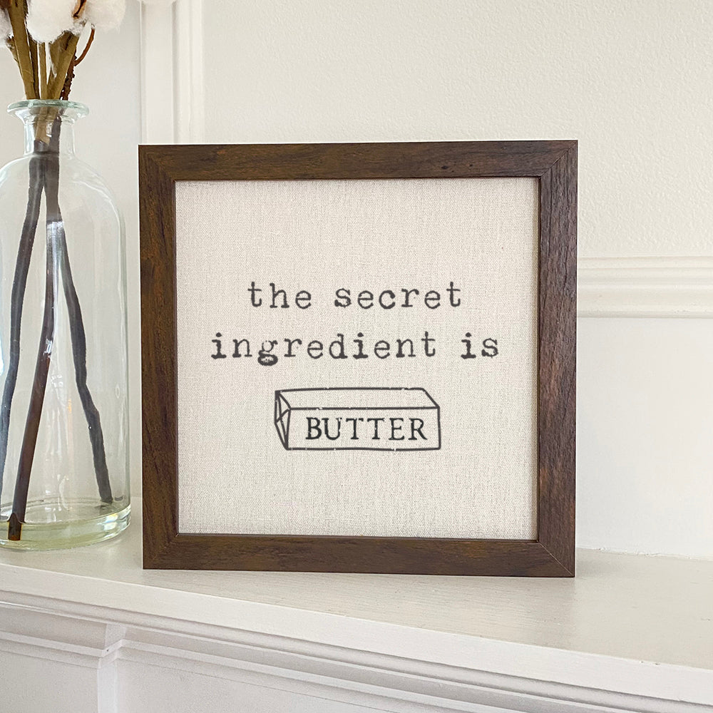 A stylish framed sign with a natural wood frame and linen-look background, featuring the words 'Secret Ingredient' in eco-friendly ink.