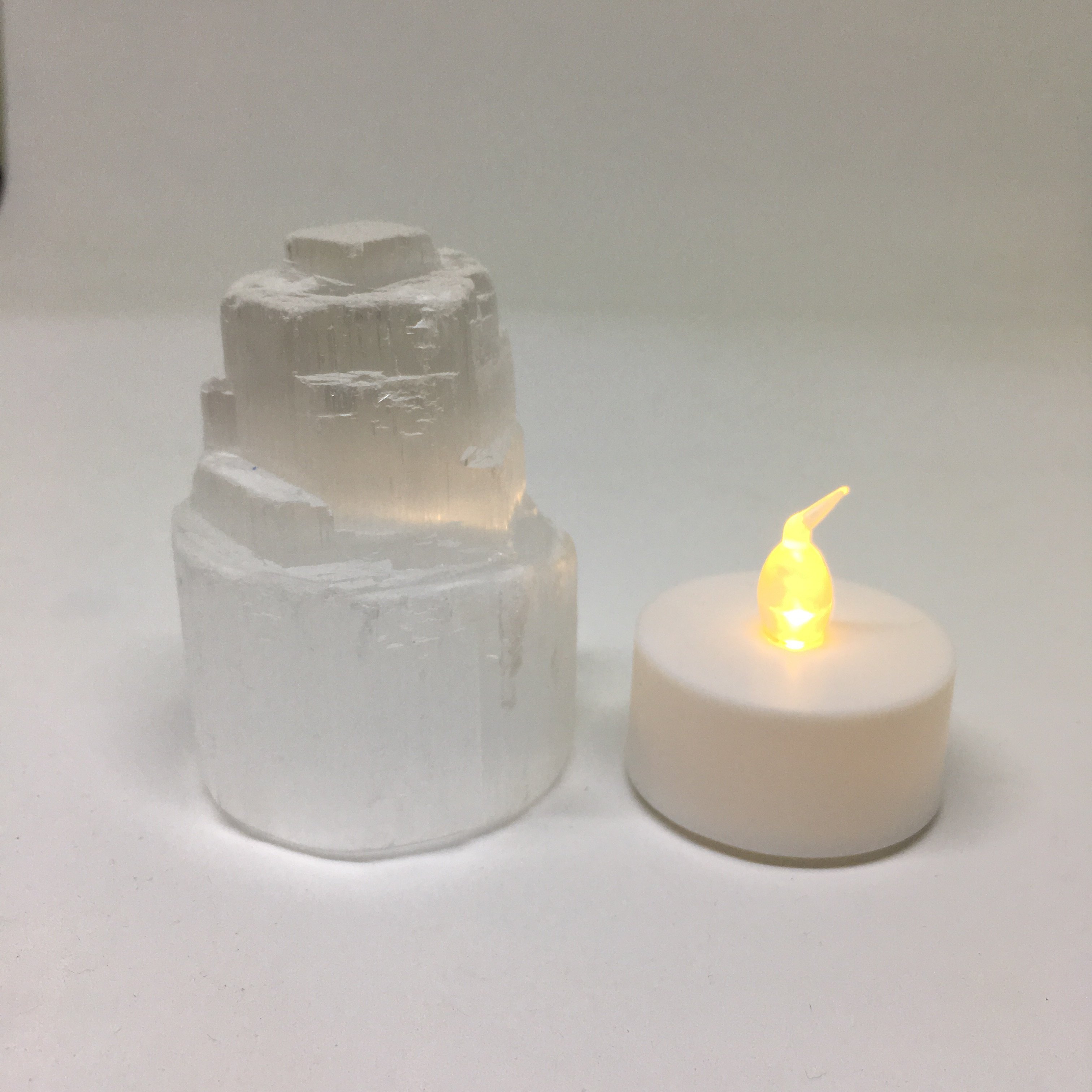 A mini Selenite skyscraper lamp with a warm yellow LED tealight, showcasing its calming and spiritual properties.