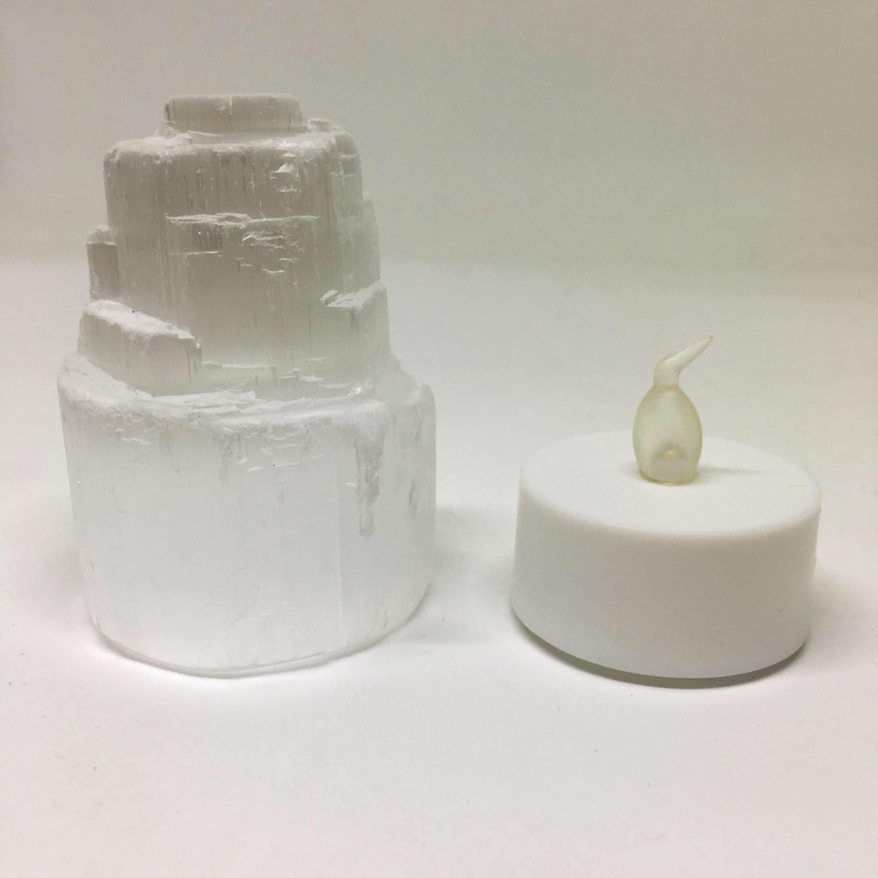 A mini Selenite skyscraper lamp with a warm yellow LED tealight, showcasing its calming and spiritual properties.