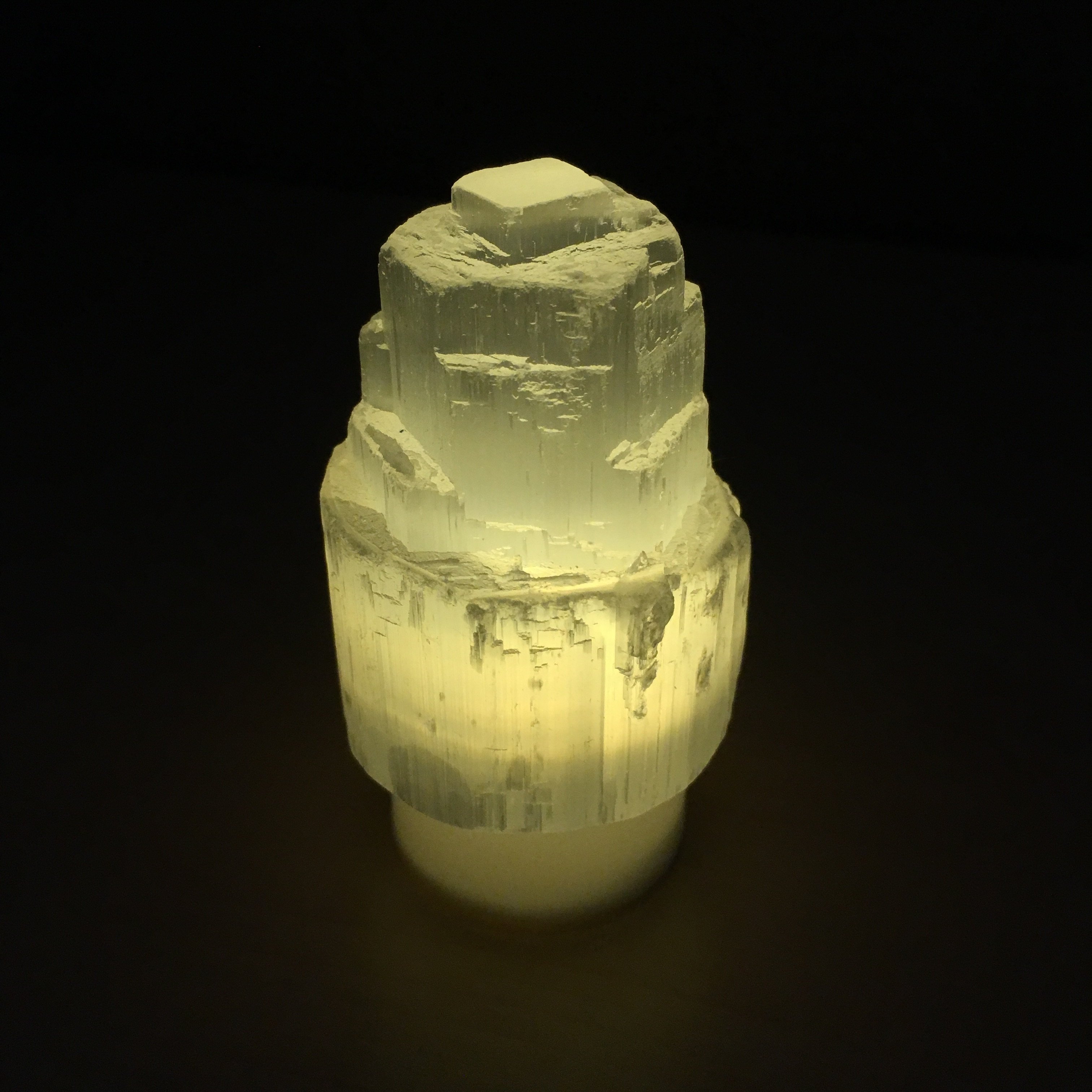 A mini Selenite skyscraper lamp with a warm yellow LED tealight, showcasing its calming and spiritual properties.