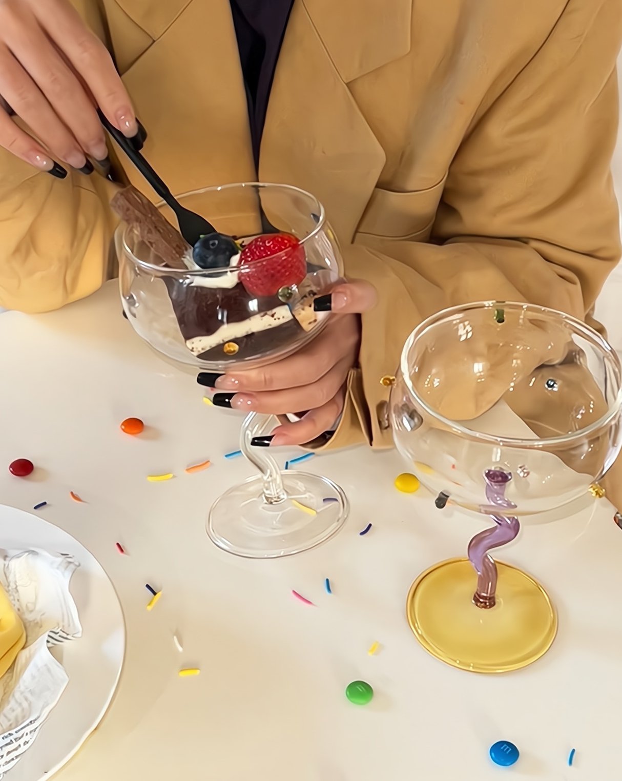 Set of 2 hand blown rainbow sprinkles wine glasses with wavy stems, one transparent and one purple, showcasing vibrant colors and elegant design.