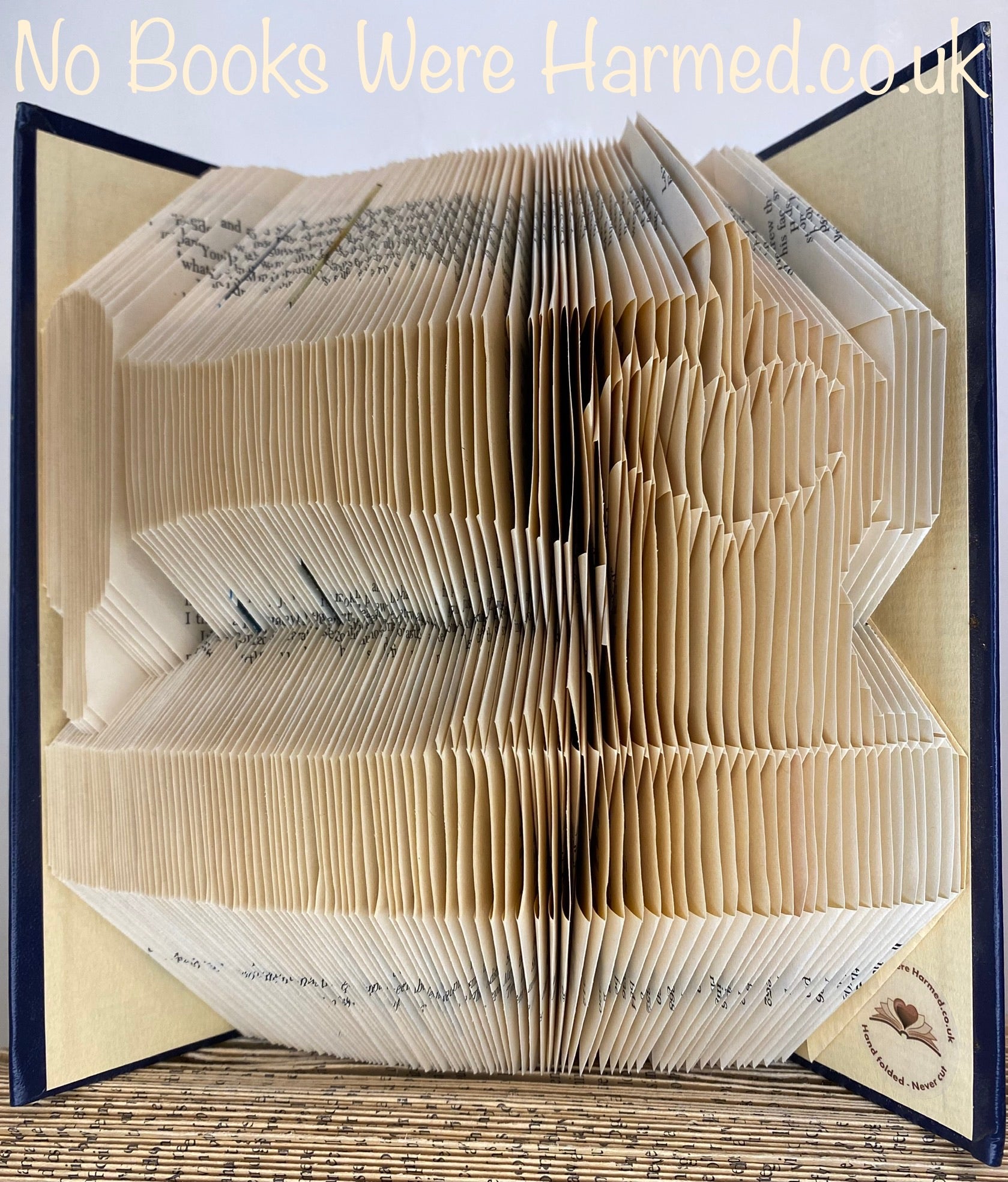 Artistic representation of a sewing machine made from hand-folded pages of vintage books, showcasing unique textures and colors.