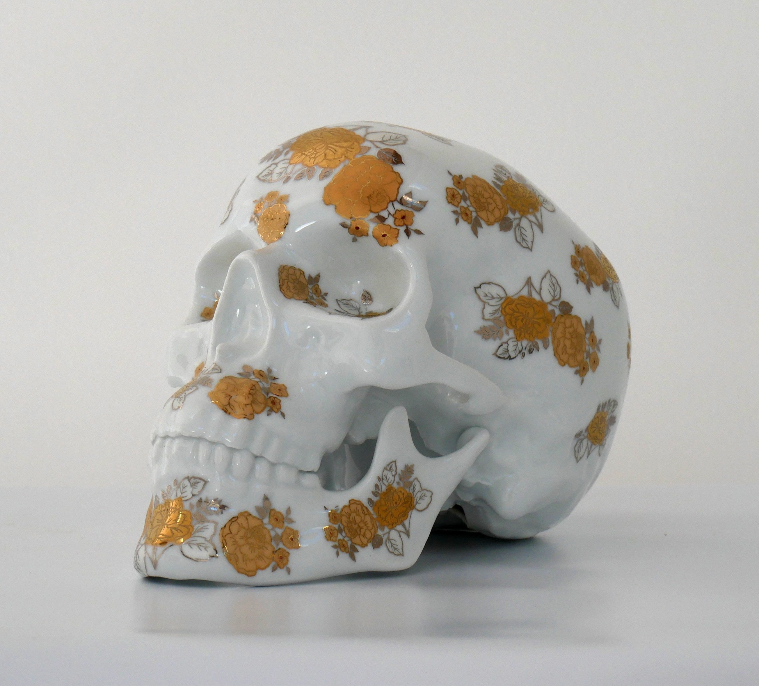 A unique Skull Gold Flowers art piece by NooN, crafted from extra white porcelain with gold floral accents, showcasing its intricate design.