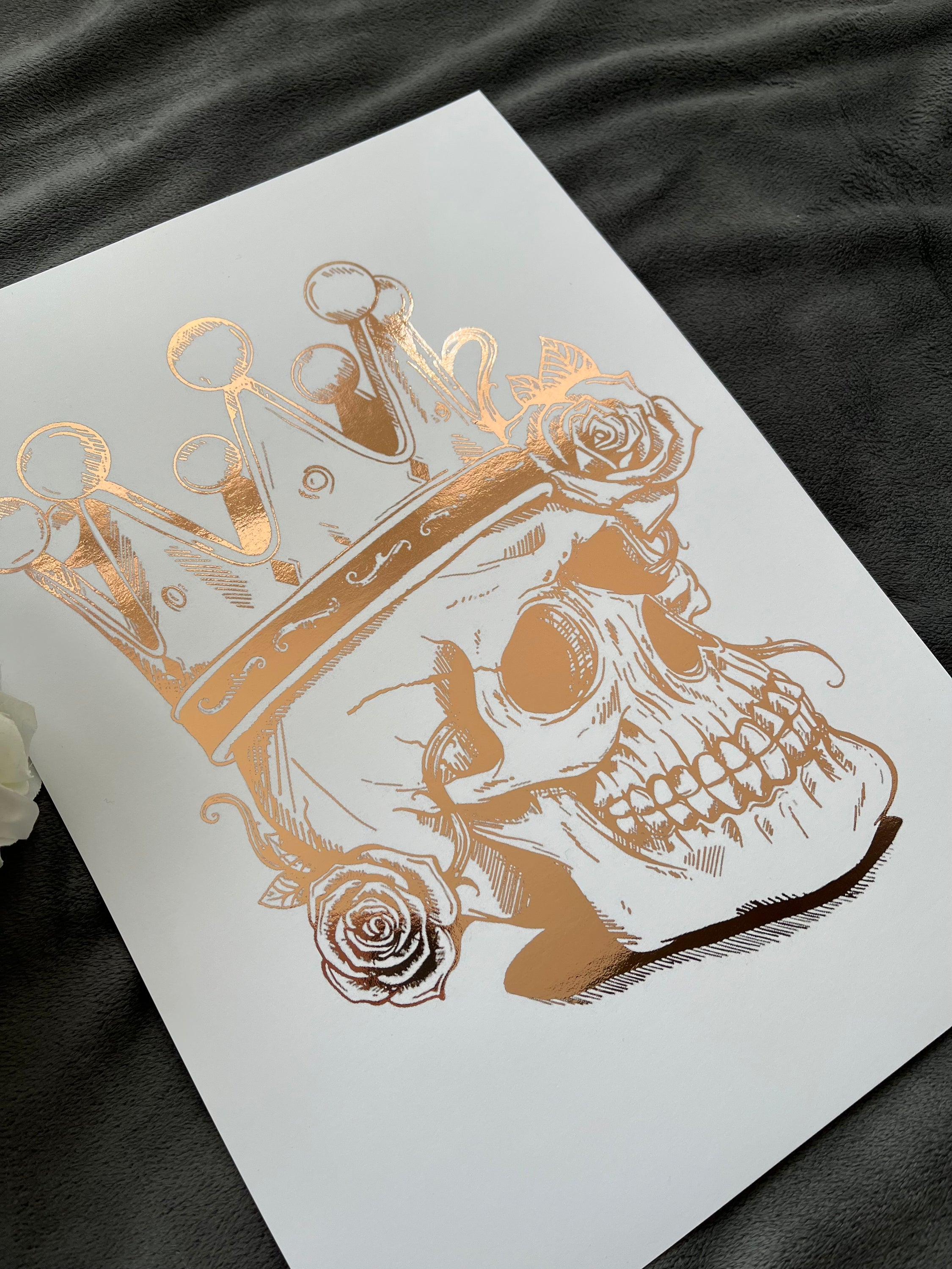 A striking rose gold foil print featuring a skull adorned with a majestic crown, showcasing intricate details and luxurious accents.