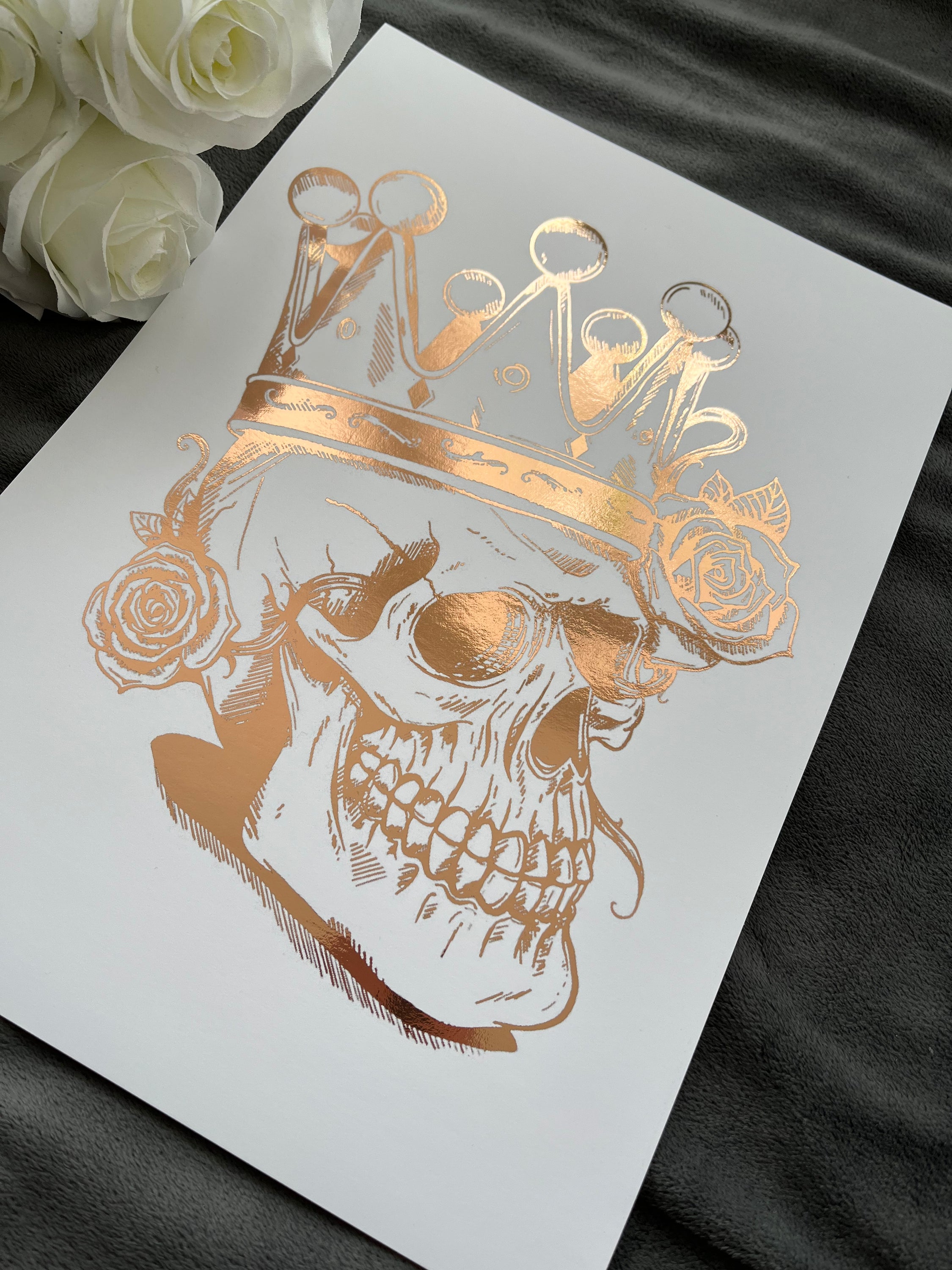 A striking rose gold foil print featuring a skull adorned with a majestic crown, showcasing intricate details and luxurious accents.