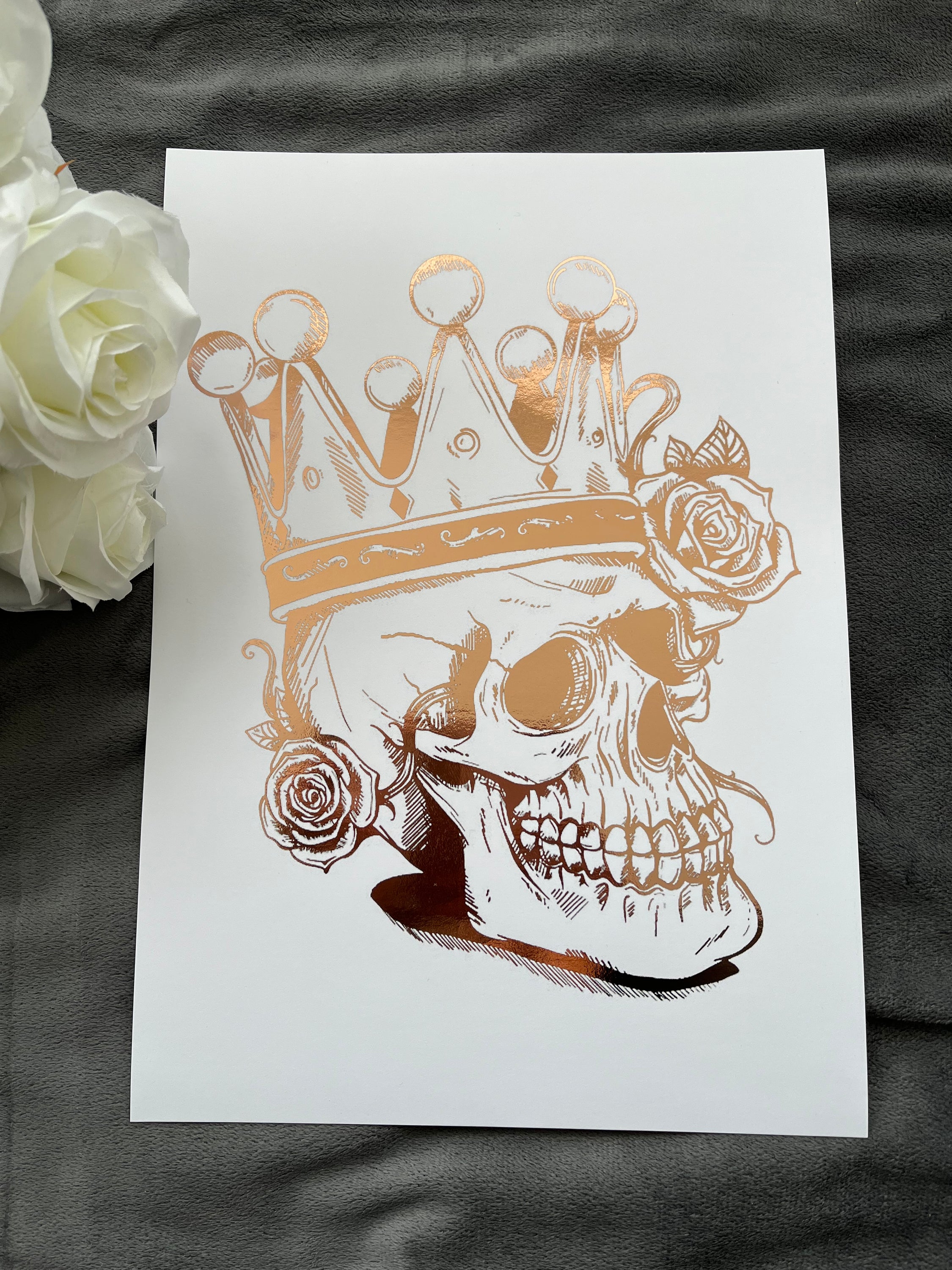 A striking rose gold foil print featuring a skull adorned with a majestic crown, showcasing intricate details and luxurious accents.