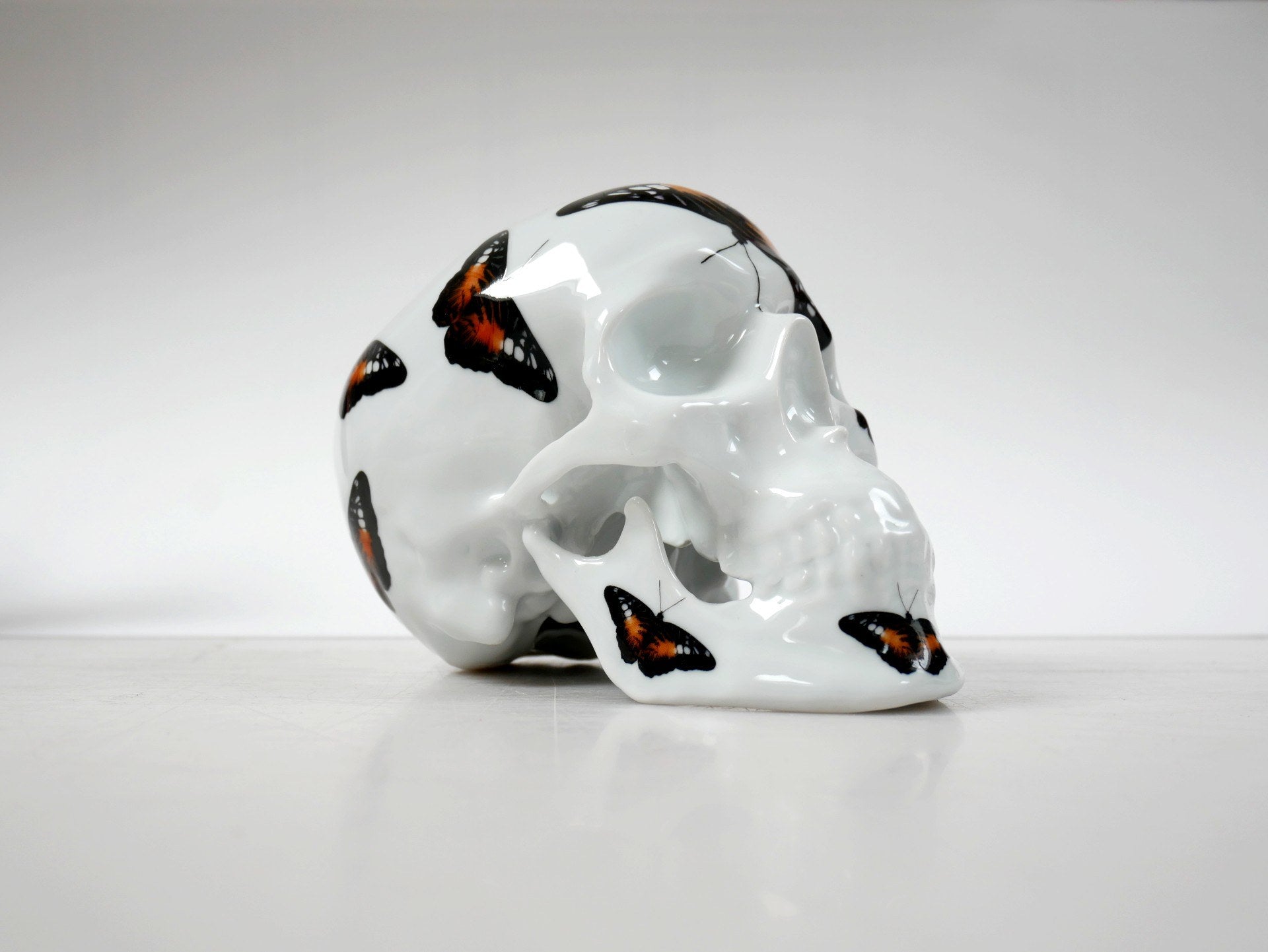 A unique Skull Orange Butterfly art piece by NooN, crafted from extra white porcelain, showcasing vibrant colors and intricate details.