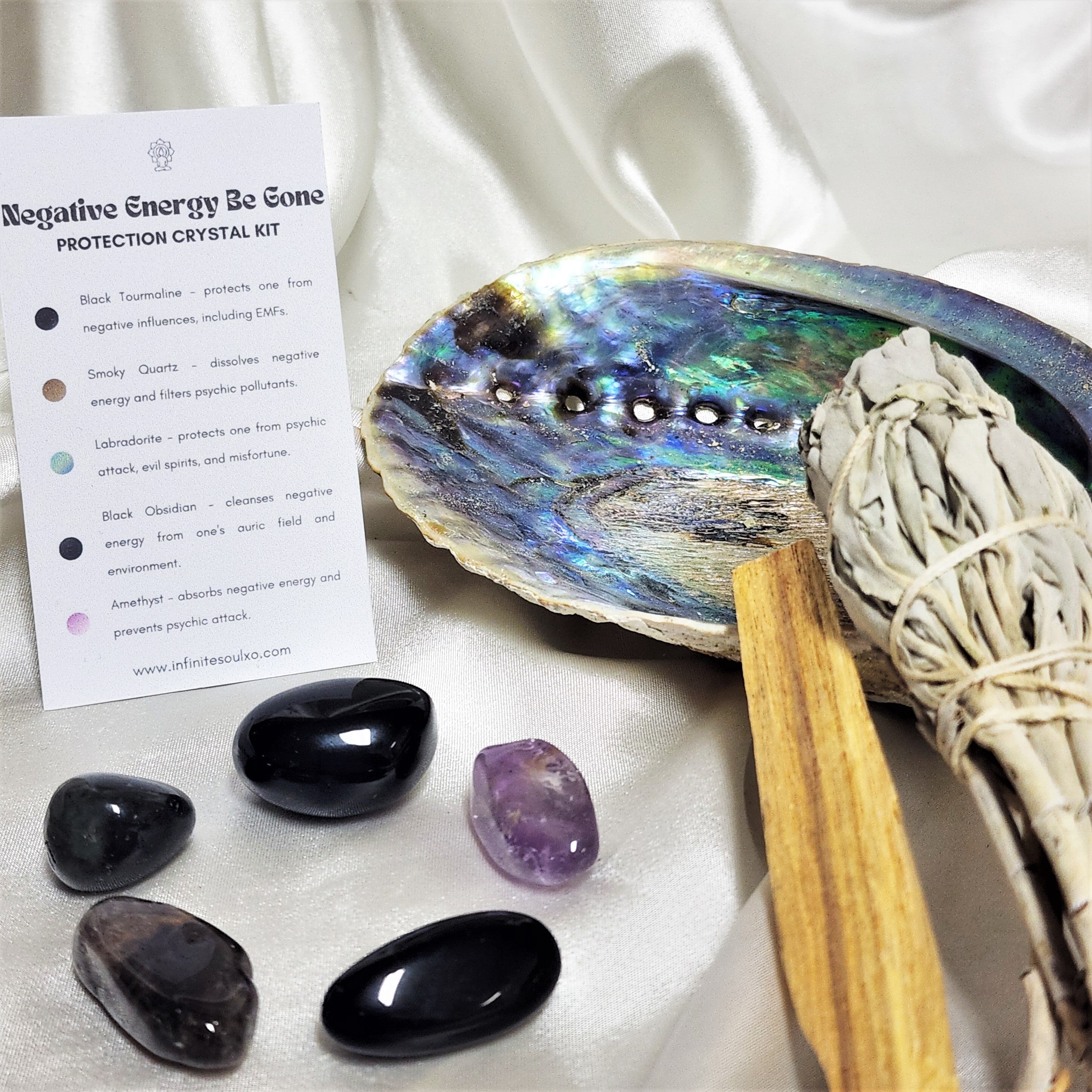 A beautifully arranged Protection Smudge Kit featuring a large sage smudge stick, palo santo wood, an abalone shell, and various protective crystals including smoky quartz and black tourmaline.