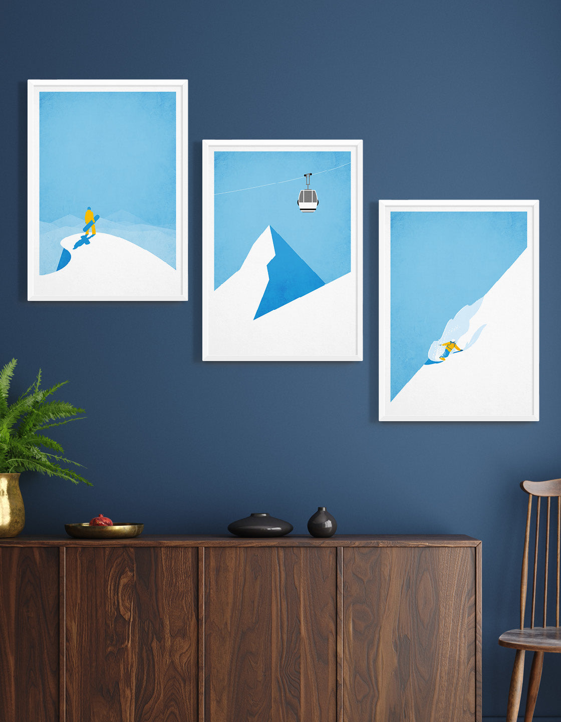 A minimalist art set of 3 posters featuring a snowboarder on a peak, a ski gondola against a blue sky, and a boarder riding powder on a mountainside.