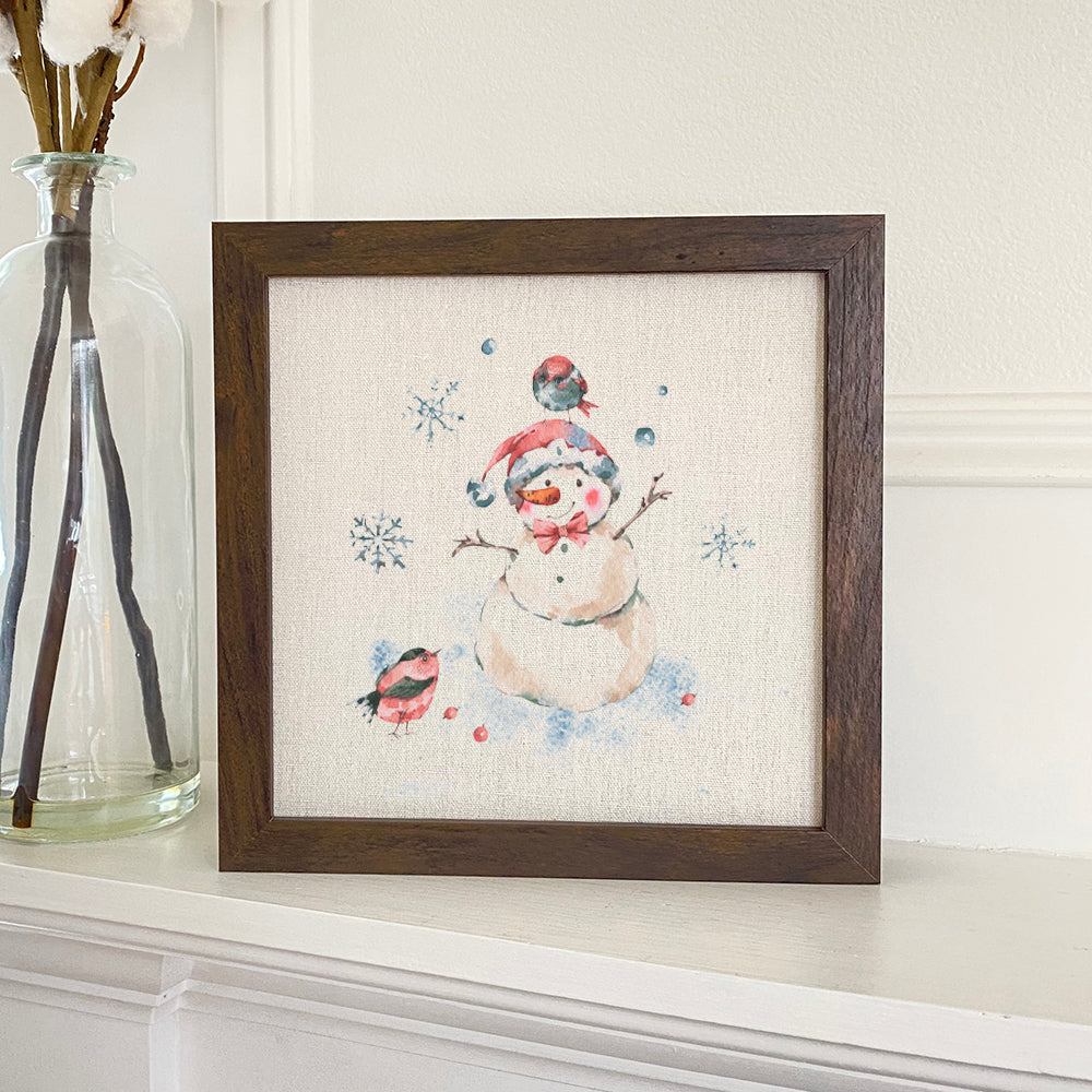 A charming framed sign featuring a snowman surrounded by birds, set in a stylish wood frame, perfect for holiday decor.