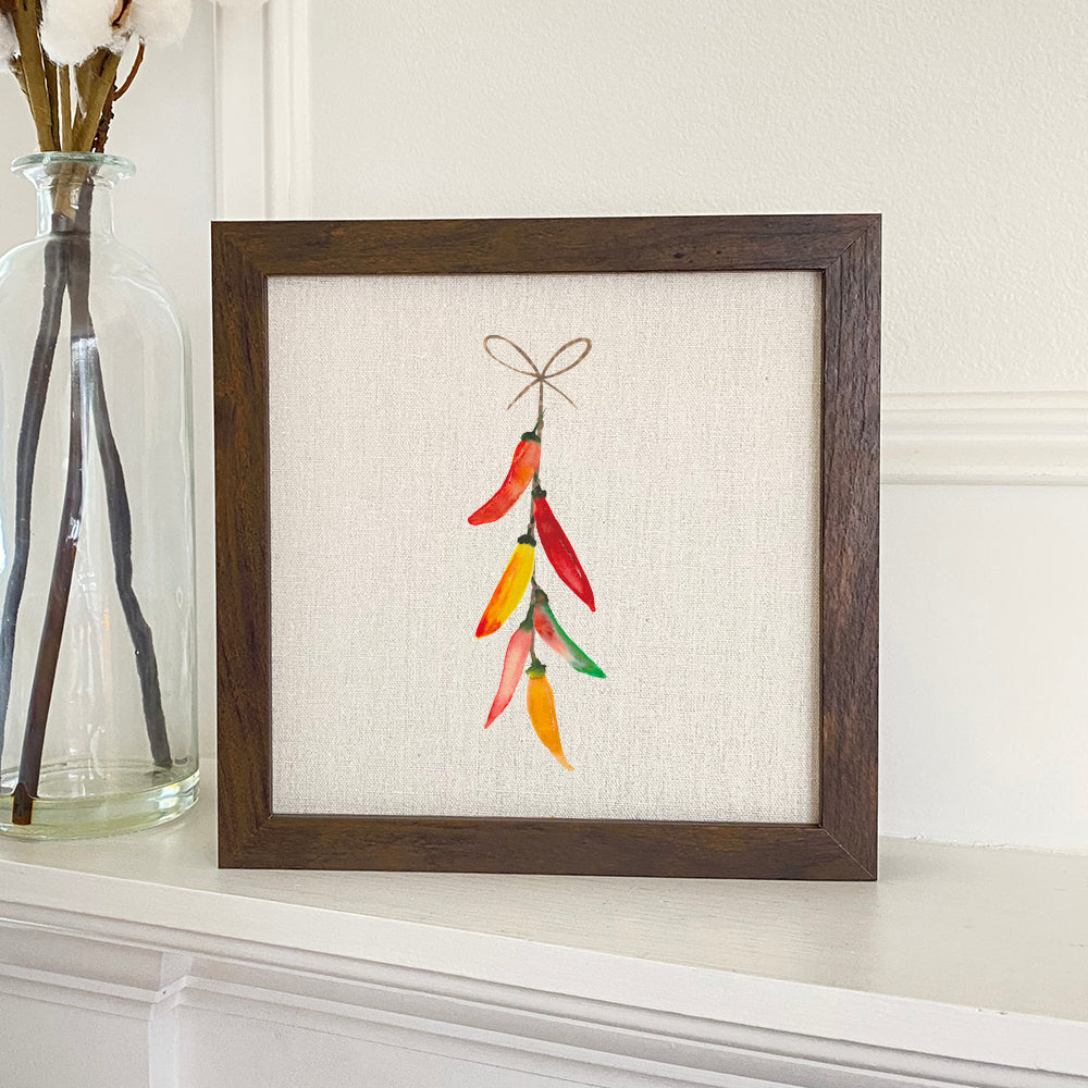 A beautifully framed sign featuring a String of Peppers design, set against a neutral linen-look background, perfect for home decor.