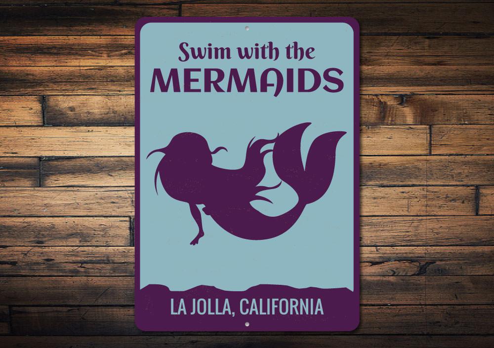 A decorative metal sign featuring the phrase 'Swim With The Mermaids', designed for beach-themed decor, showcasing vibrant colors and a whimsical design.