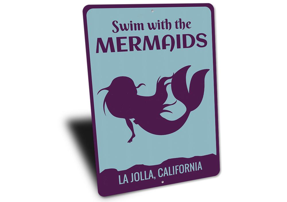 A decorative metal sign featuring the phrase 'Swim With The Mermaids', designed for beach-themed decor, showcasing vibrant colors and a whimsical design.