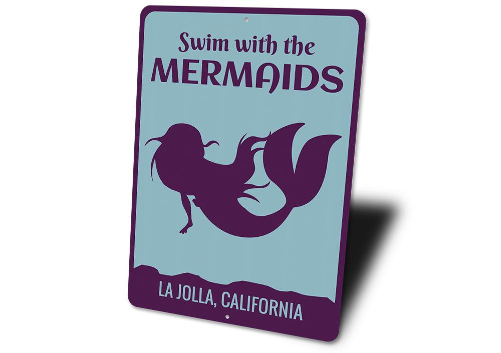 A decorative metal sign featuring the phrase 'Swim With The Mermaids', designed for beach-themed decor, showcasing vibrant colors and a whimsical design.