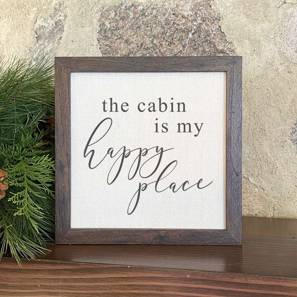 Framed sign reading 'The Cabin is my Happy Place' with a stylish wood frame and linen-look background.