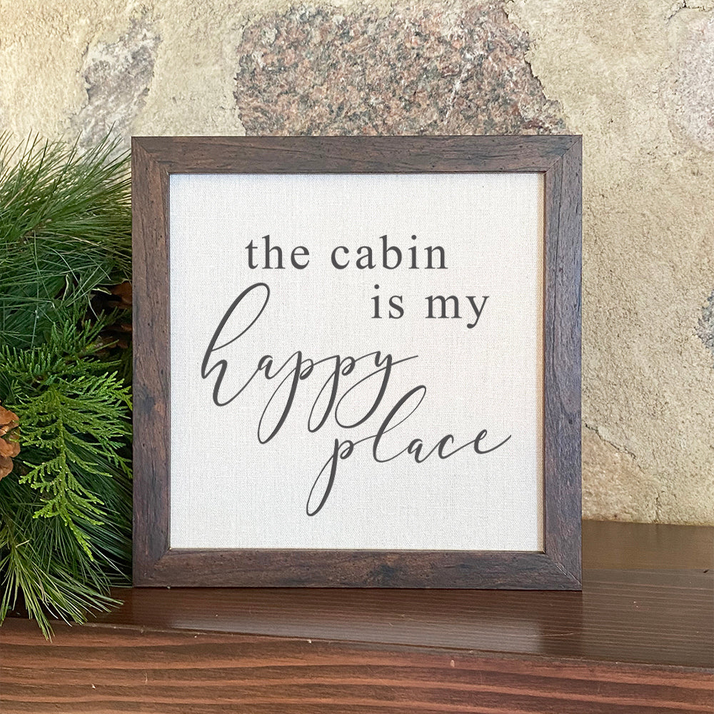 Framed sign reading 'The Cabin is my Happy Place' with a stylish wood frame and linen-look background.