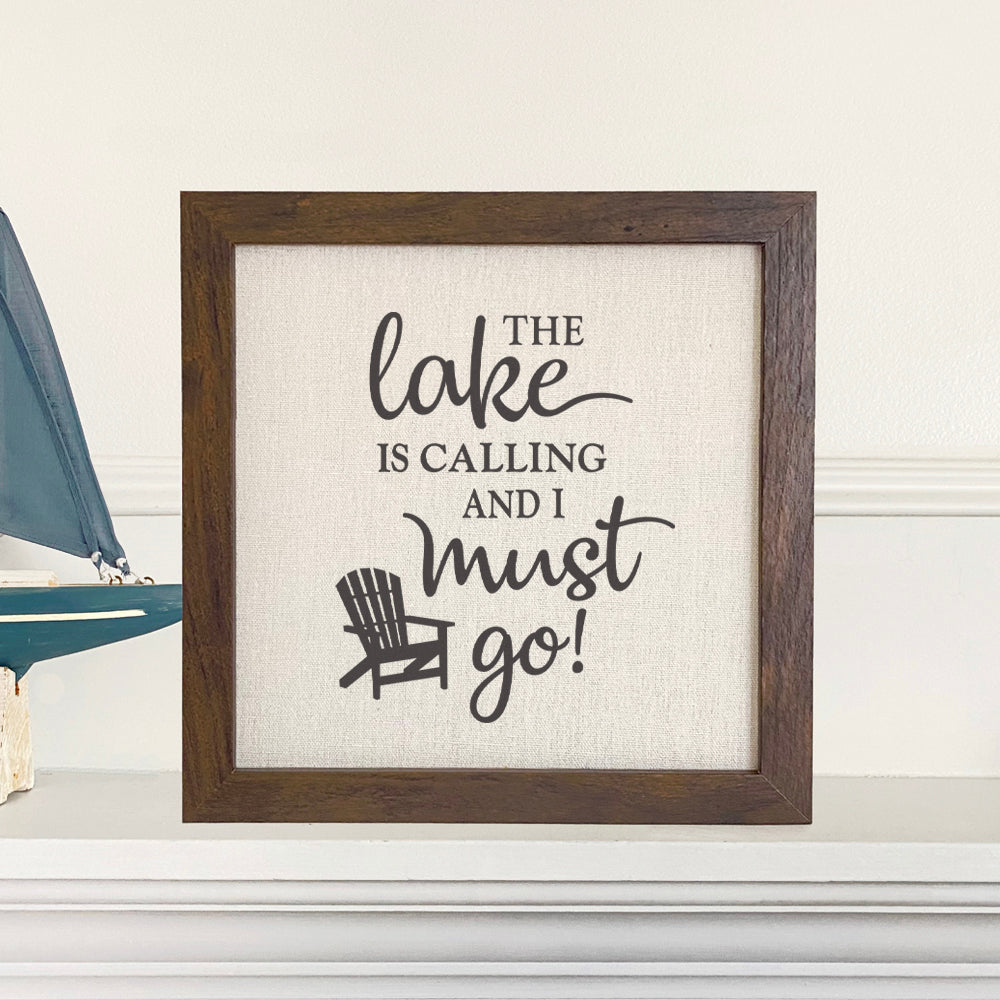 Framed sign featuring 'The Lake is Calling' with a stylish wood frame and linen-look background, perfect for home decor.