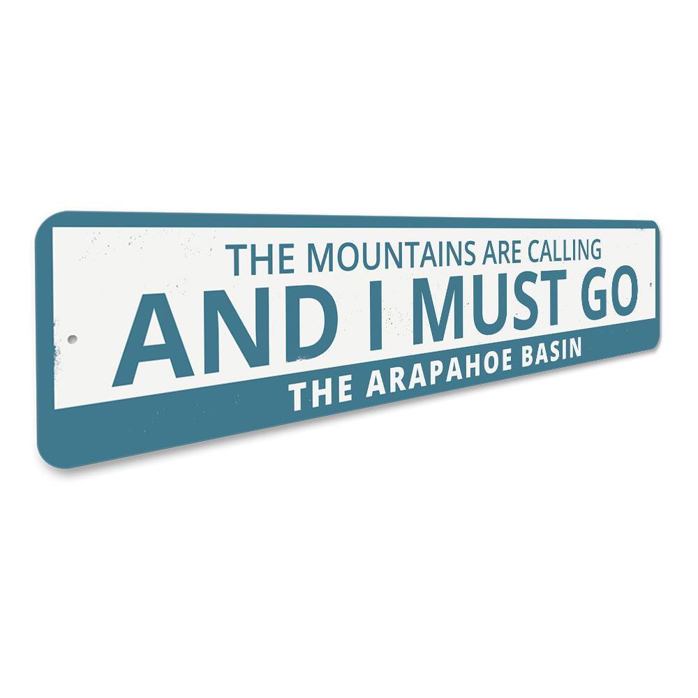 A decorative aluminum sign featuring the phrase 'The Mountains Are Calling and I Must Go', perfect for ski lovers and outdoor enthusiasts.