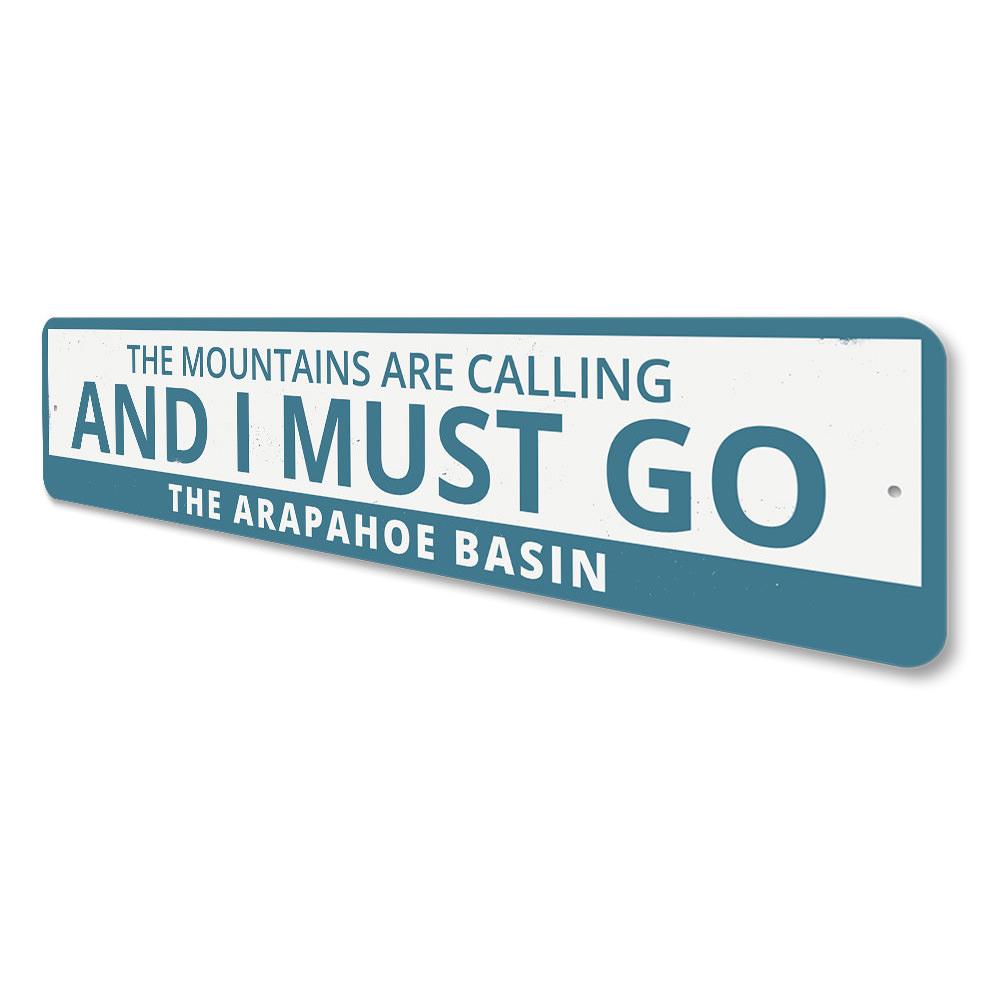 A decorative aluminum sign featuring the phrase 'The Mountains Are Calling and I Must Go', perfect for ski lovers and outdoor enthusiasts.