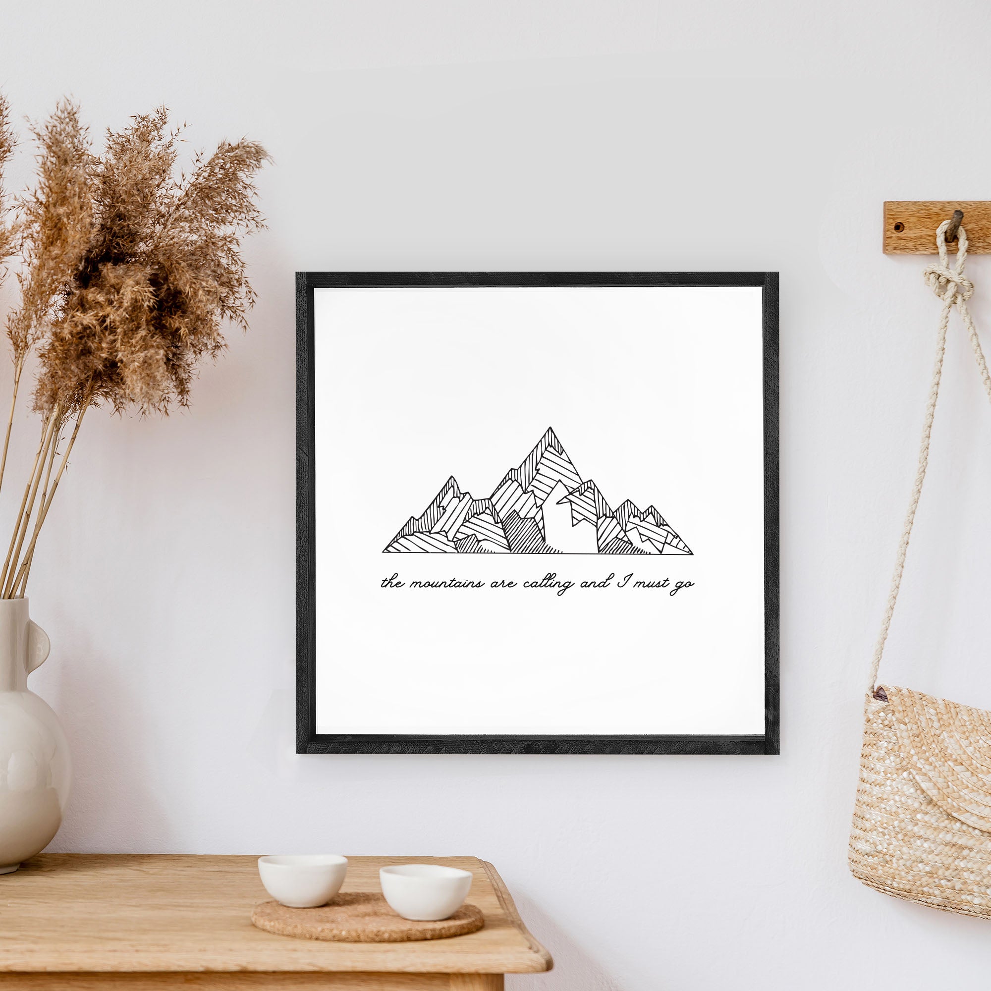 A rustic wood sign featuring the phrase 'The Mountains Are Calling And I Must Go' with a white background and black waterproof text, framed in stained pine wood.