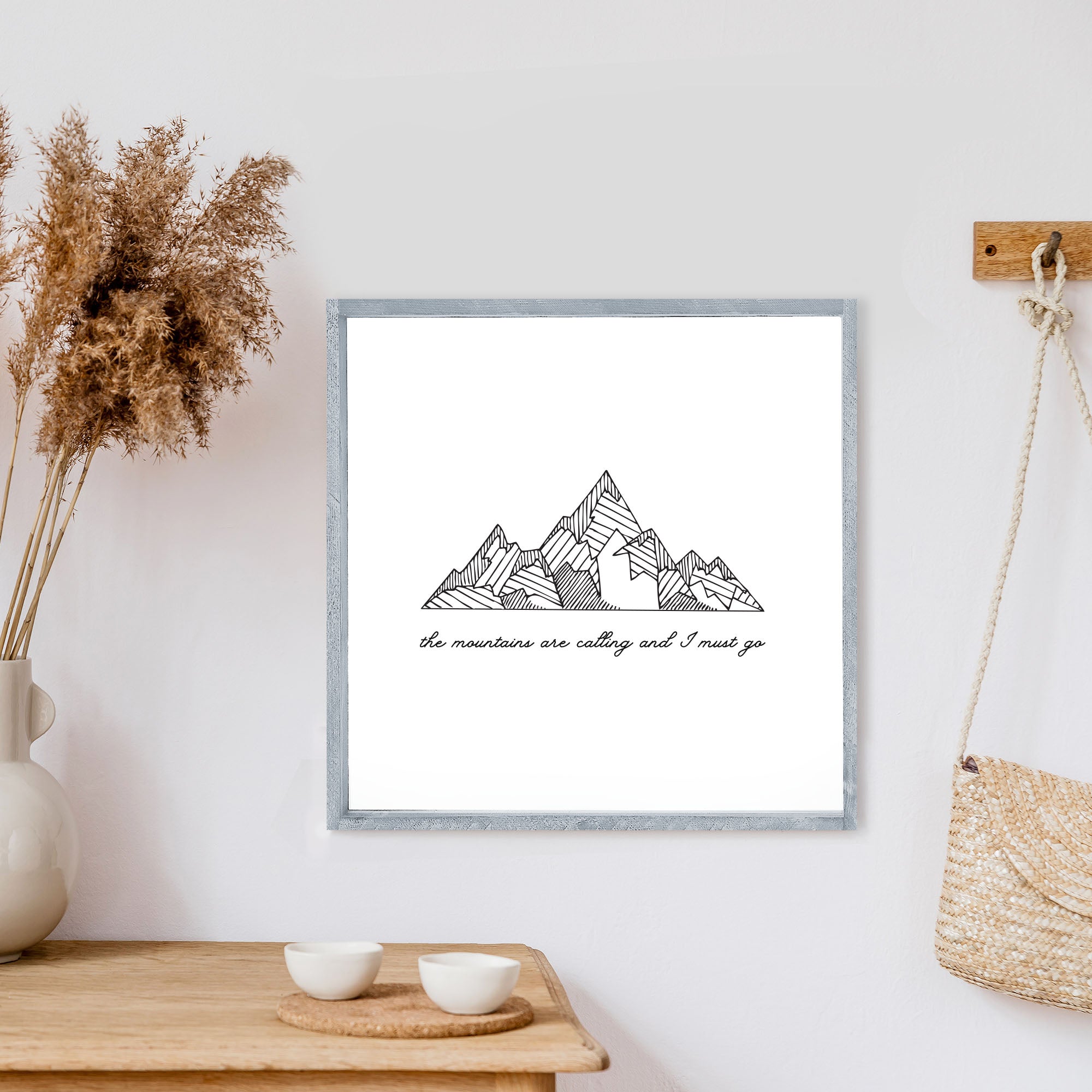 A rustic wood sign featuring the phrase 'The Mountains Are Calling And I Must Go' with a white background and black waterproof text, framed in stained pine wood.