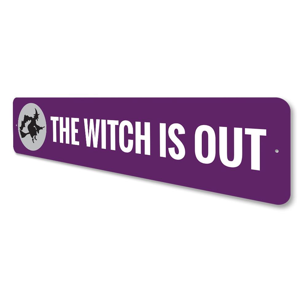 A decorative Halloween sign reading 'The Witch is OUT', made of high-quality aluminum, featuring spooky design elements.