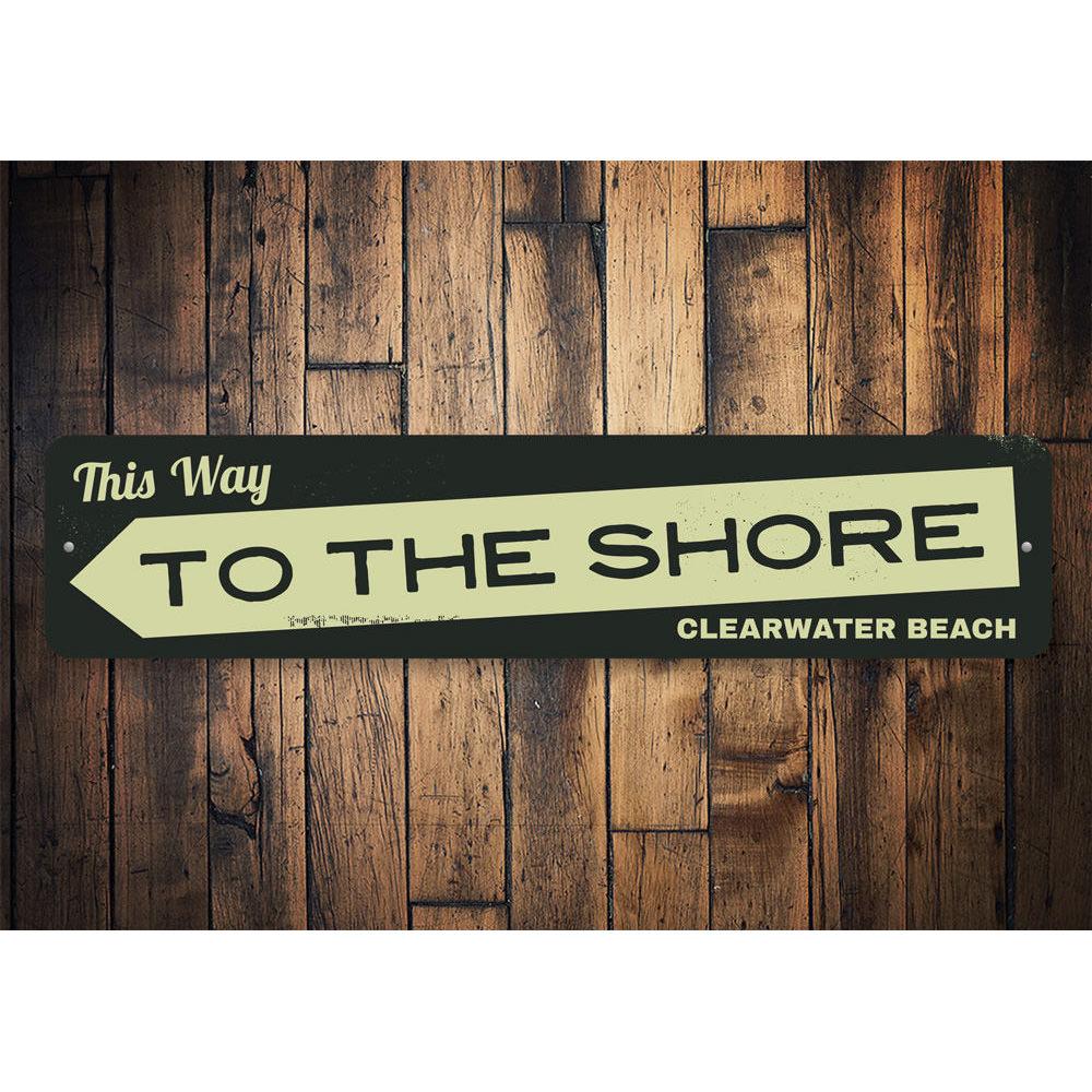 A decorative metal sign reading 'This Way to the Shore', featuring a coastal design, perfect for beach houses and coastal decor.