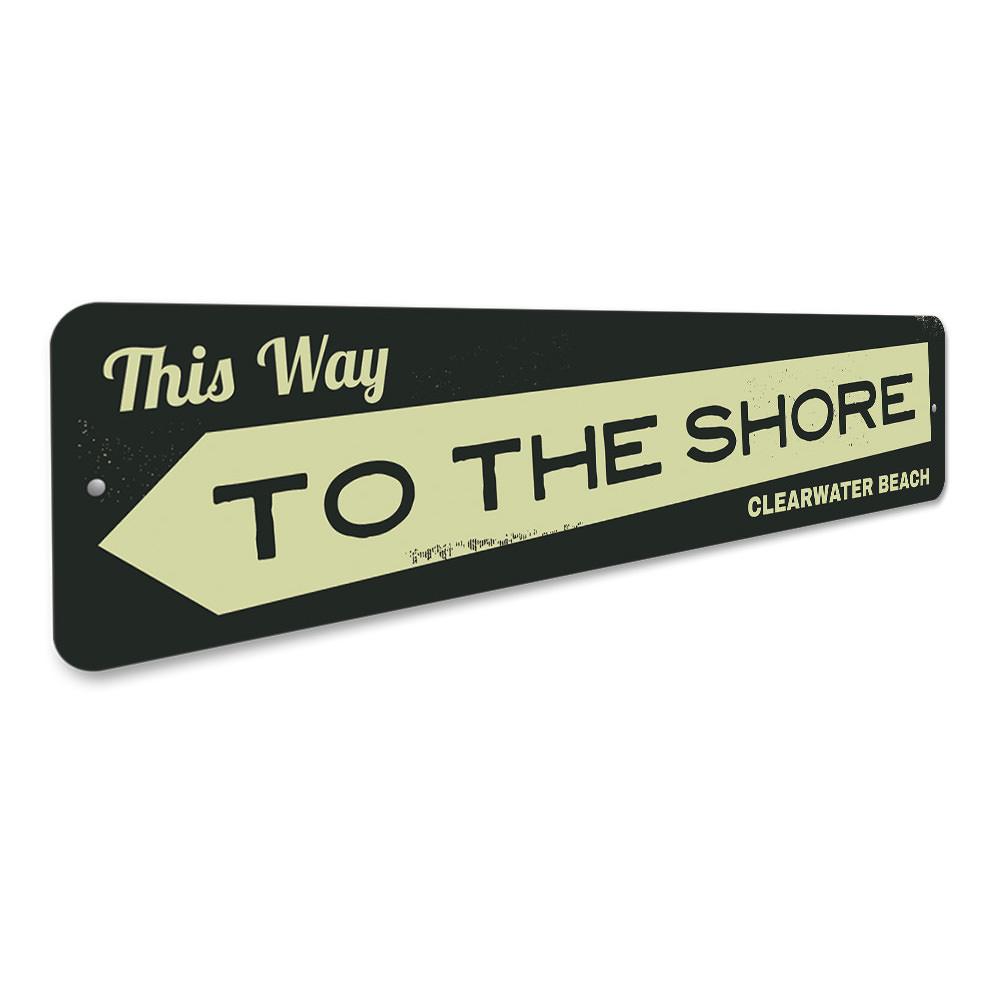 A decorative metal sign reading 'This Way to the Shore', featuring a coastal design, perfect for beach houses and coastal decor.