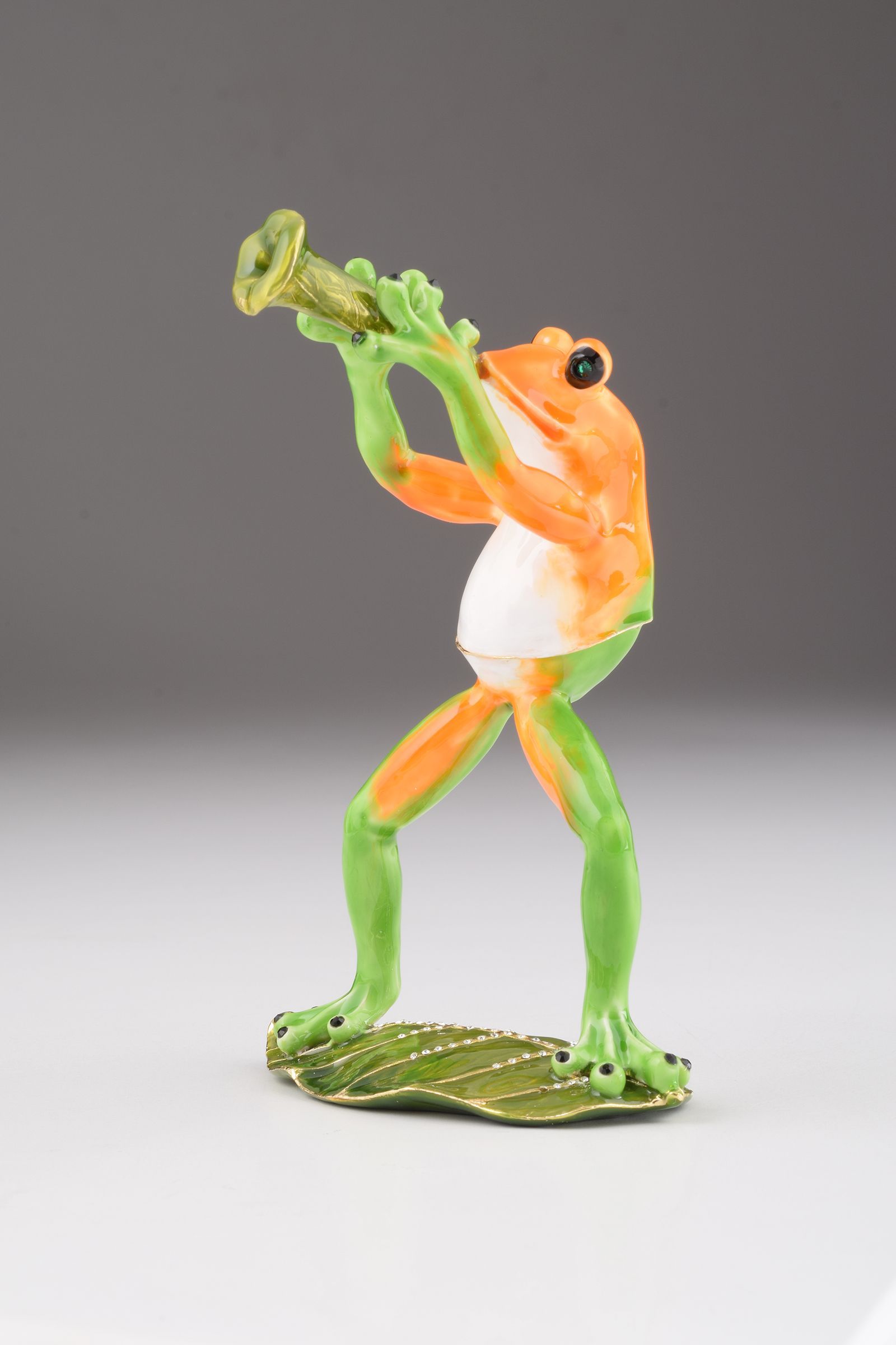 A beautifully crafted Trumpet Playing Frog trinket box, featuring vibrant enamel and sparkling Austrian crystals, plated with 24K gold.