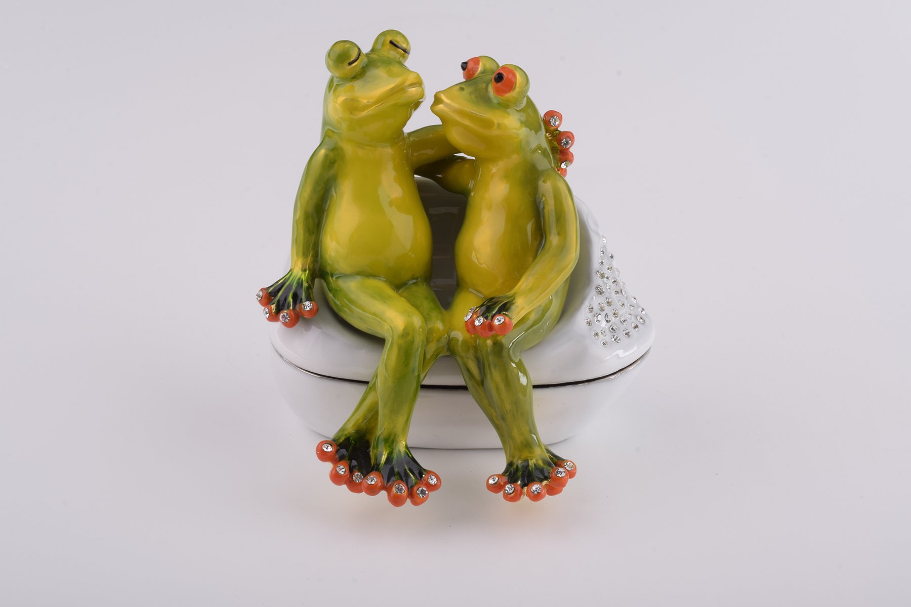 A beautifully crafted enamel trinket box featuring two frogs in love, adorned with sparkling Austrian crystals and plated with 24K gold.