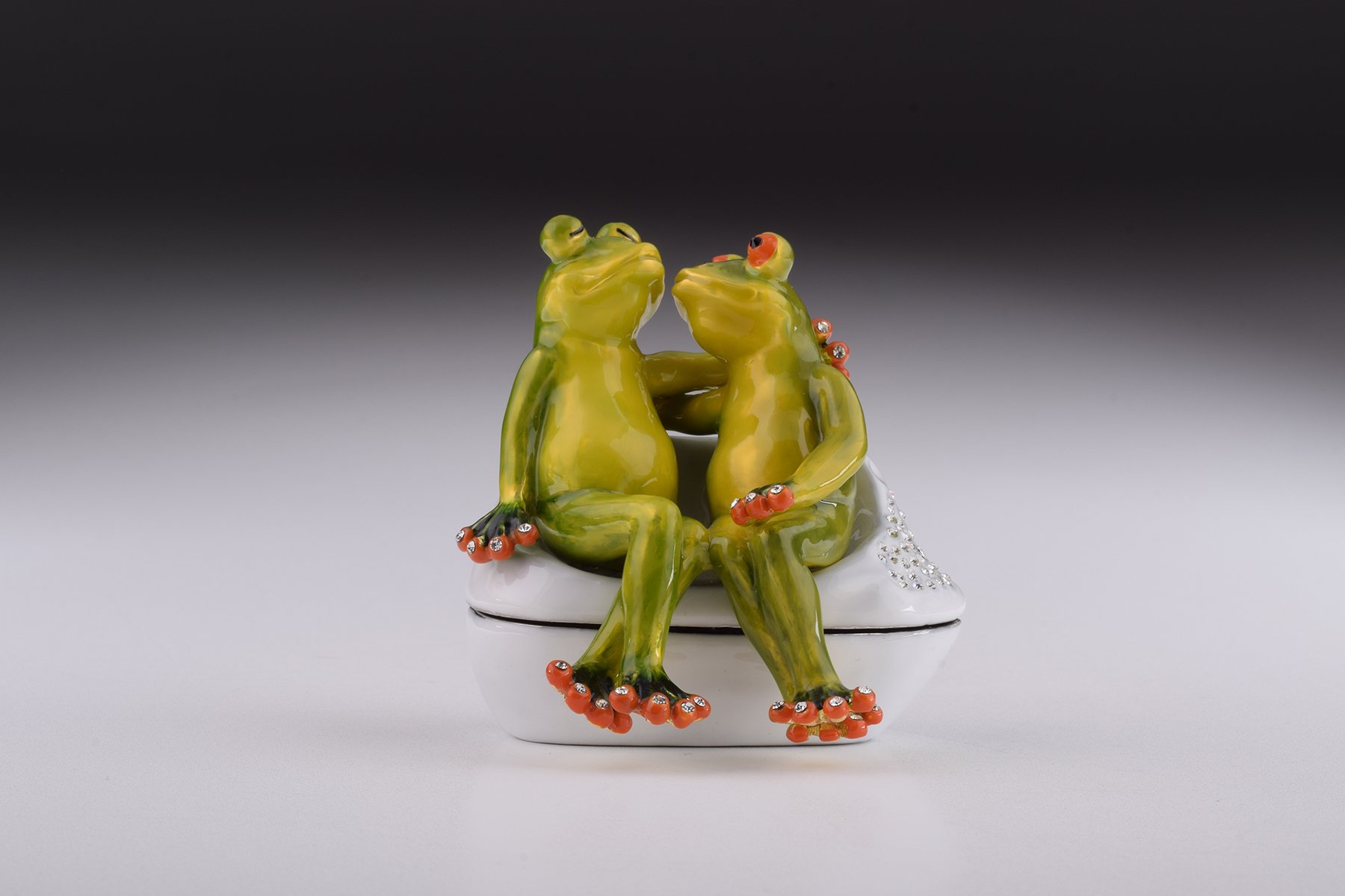 A beautifully crafted enamel trinket box featuring two frogs in love, adorned with sparkling Austrian crystals and plated with 24K gold.