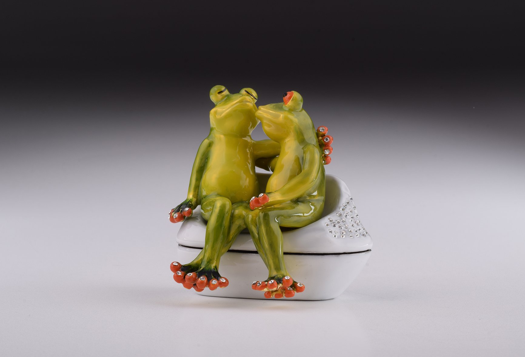 A beautifully crafted enamel trinket box featuring two frogs in love, adorned with sparkling Austrian crystals and plated with 24K gold.