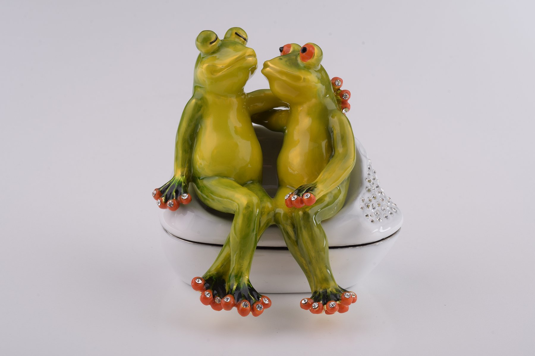 A beautifully crafted enamel trinket box featuring two frogs in love, adorned with sparkling Austrian crystals and plated with 24K gold.