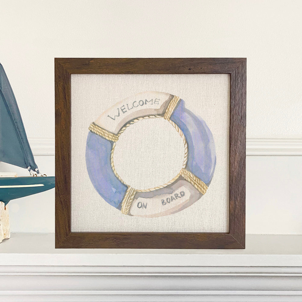 Welcome on Board Lifebuoy framed sign with a wood frame, eco-friendly printing, and a linen-look background, available in walnut or white-washed finish.