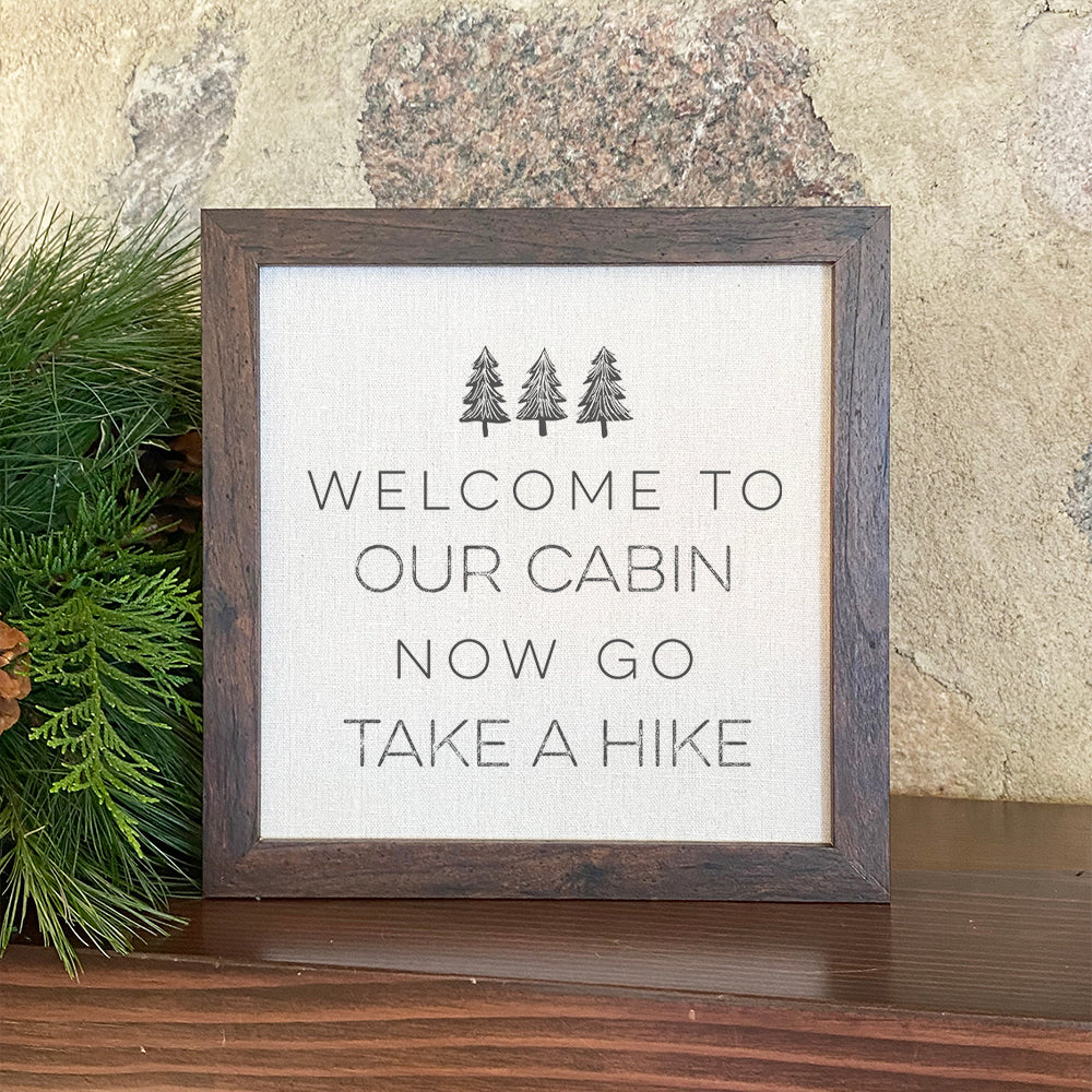 Framed sign featuring a cabin design with a wood frame, suitable for shelf or wall display.