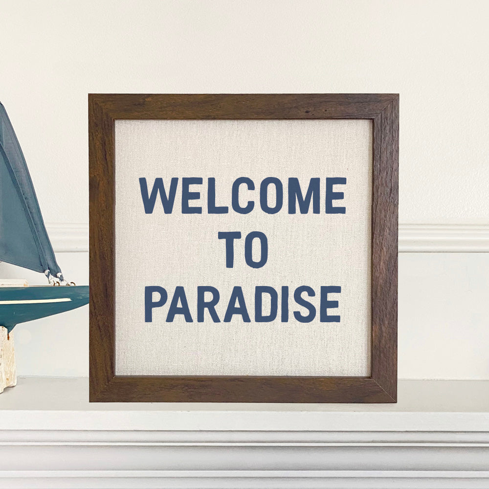 Welcome to Paradise framed sign with a stylized wood frame, eco-friendly ink printing on a linen-look background.