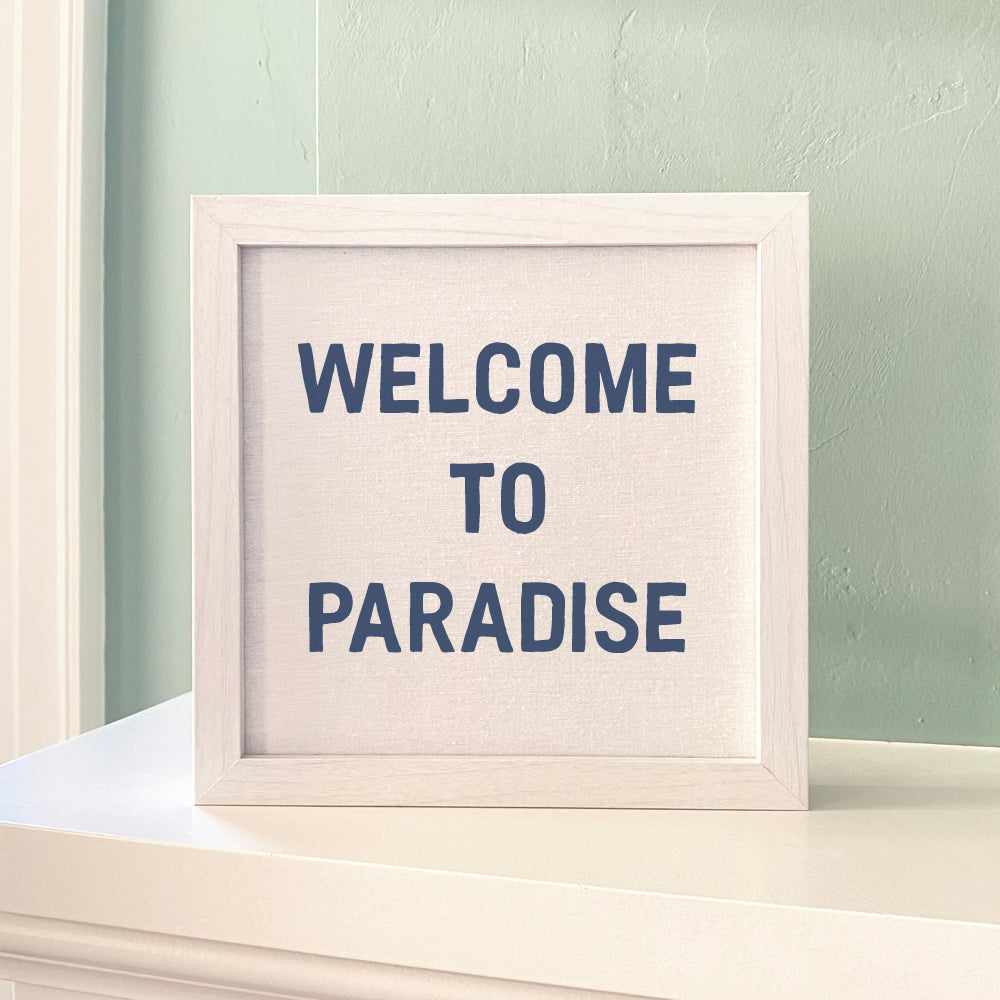 Welcome to Paradise framed sign with a stylized wood frame, eco-friendly ink printing on a linen-look background.