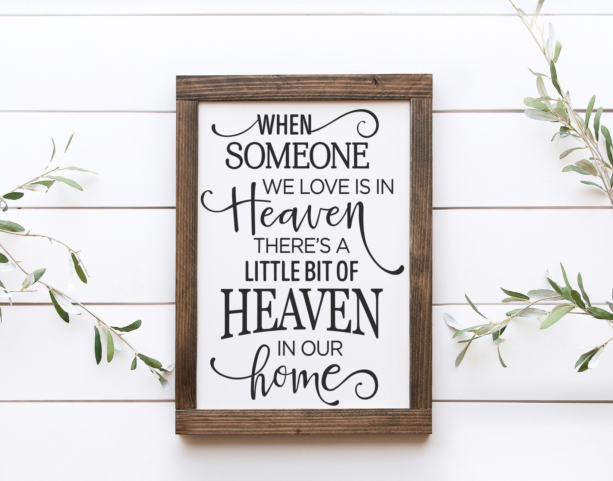 A handmade wooden sign with the phrase 'When Someone We Love Is In Heaven There Is A Little Bit Of Heaven In Our Home' painted in elegant lettering on a matte white background.