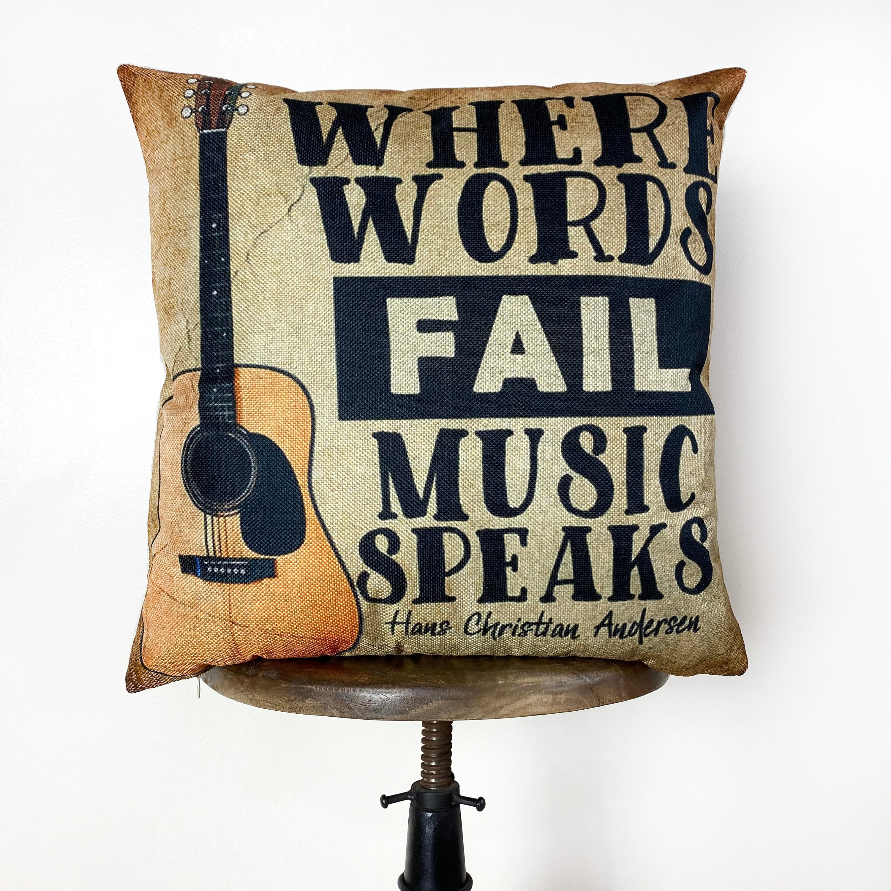 A decorative pillow cover featuring the quote 'Where Words Fail, Music Speaks' in bold letters on a gold background, perfect for music lovers.