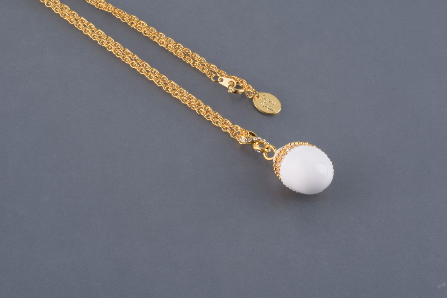 Elegant White Egg Pendant Necklace with hand-painted enamel and Austrian crystals, plated with 24K gold, displayed on a soft background.