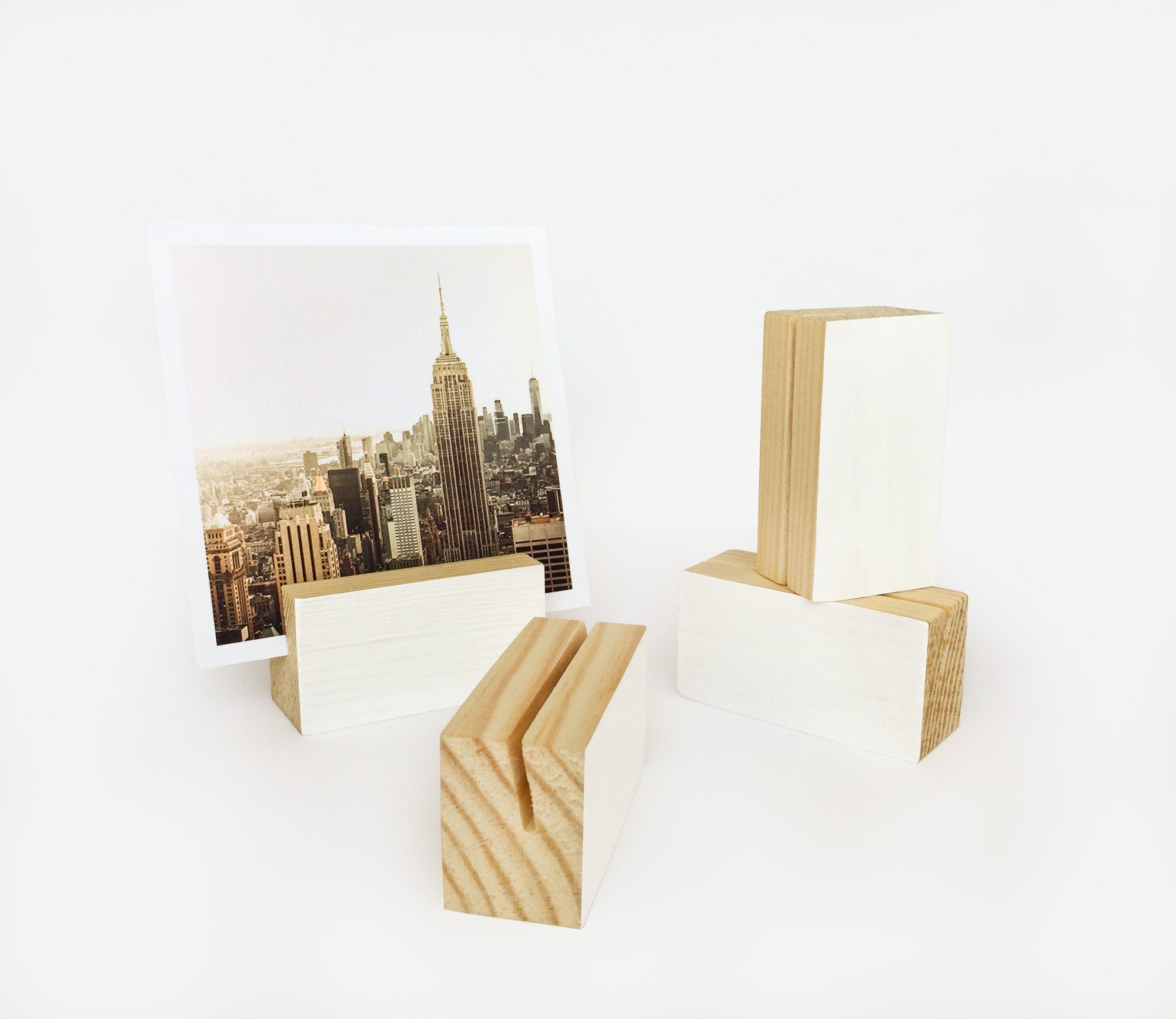 A white wood block holder displaying various small art prints and photos, showcasing its elegant design and eco-friendly craftsmanship.