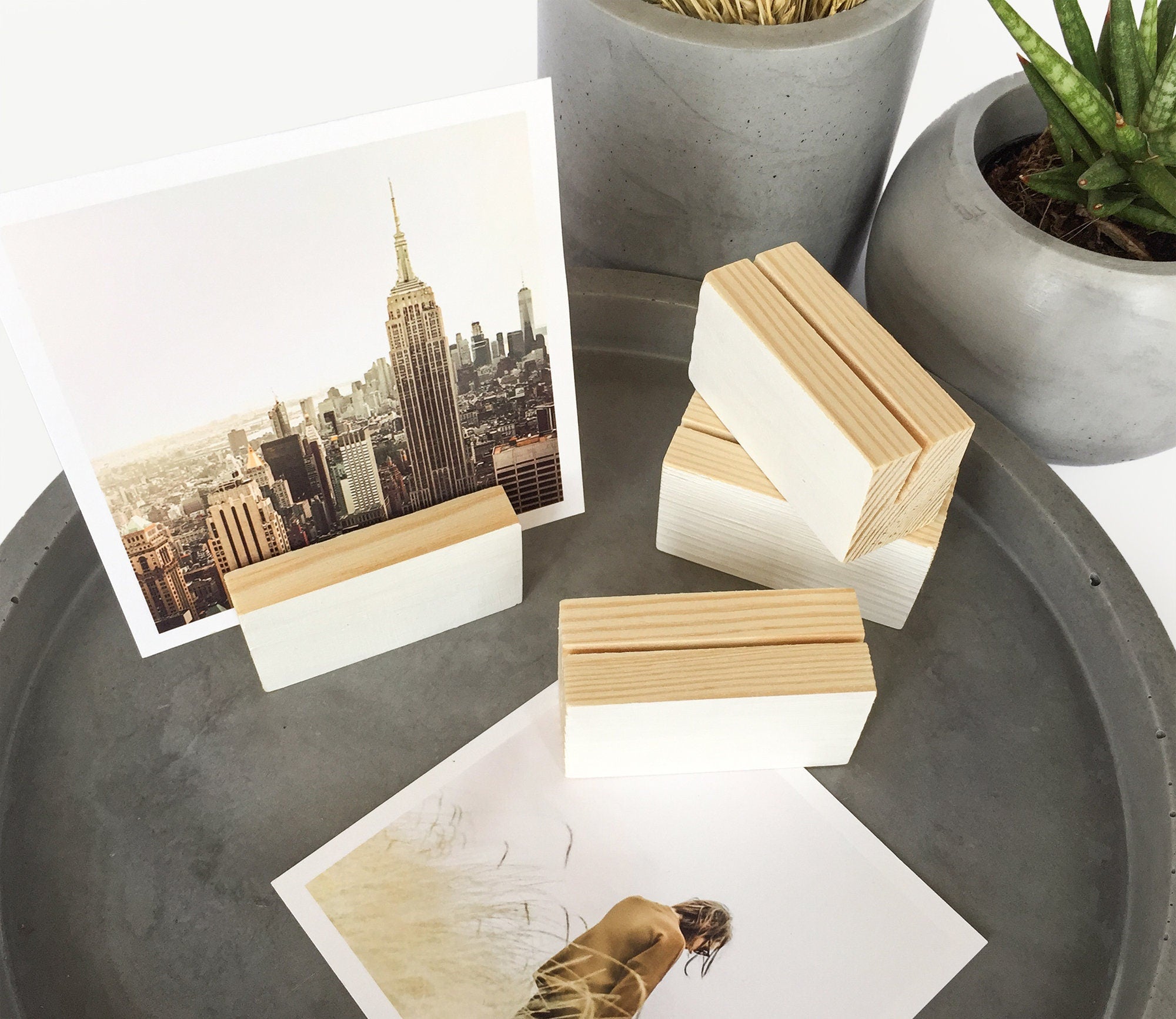 A white wood block holder displaying various small art prints and photos, showcasing its elegant design and eco-friendly craftsmanship.