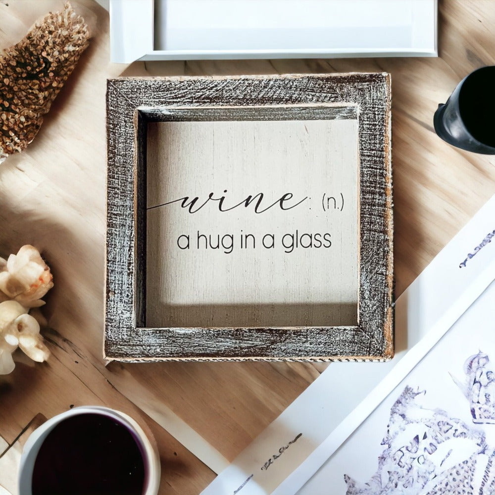 A beautifully framed wooden sign that reads 'Wine: A Hug', featuring a white-washed finish, perfect for home decor.